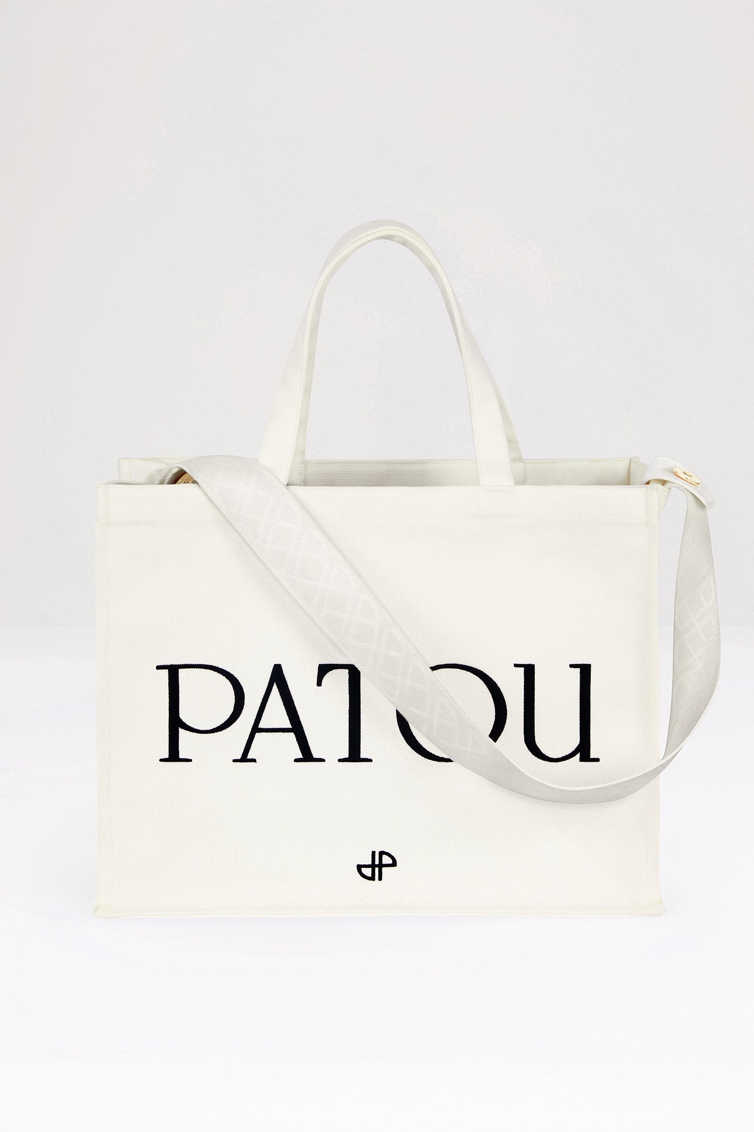 Patou - Patou canvas tote in organic cotton - Cream - Carry your Patou everywhere with you. Cream organic cotton tote. Patou lettering logo and JP monogram in black. White embossed shoulder strap with gold buttons. Two top handles. Can be carried by hand or on the shoulder.