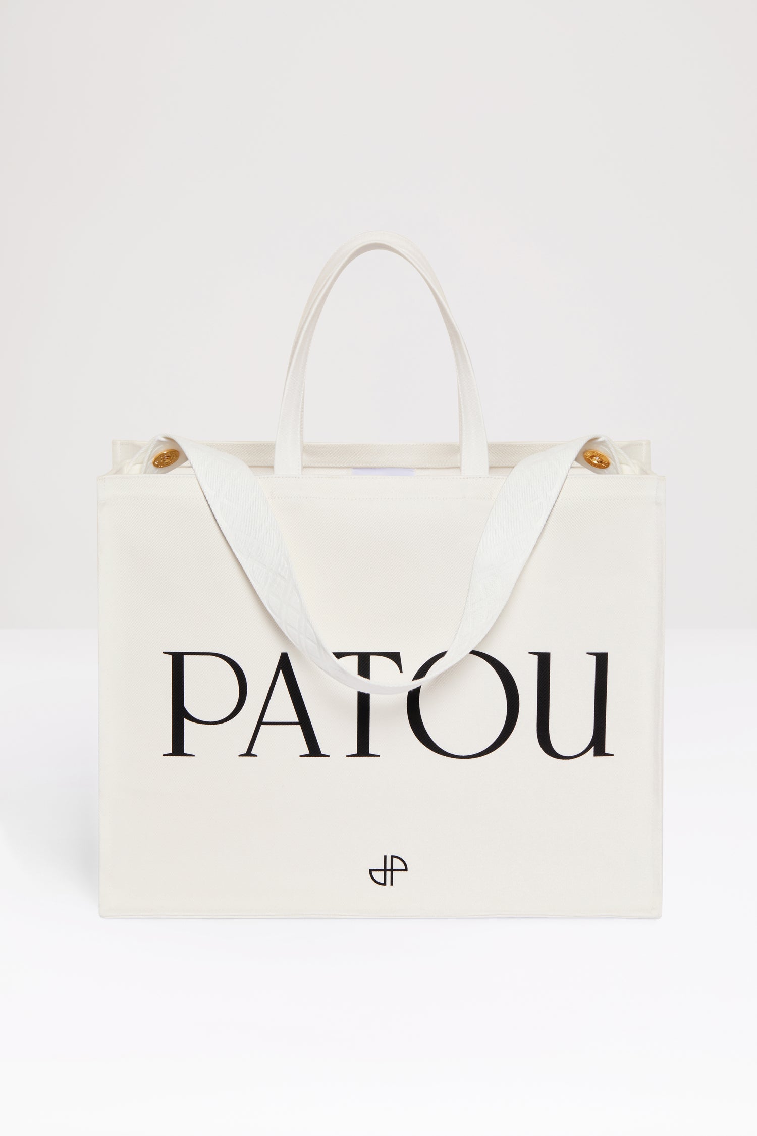 Patou - Patou canvas tote in organic cotton - Cream - Carry your Patou everywhere with you. Cream organic cotton tote. Patou lettering logo and JP monogram in black. White embossed shoulder strap with gold buttons. Two top handles. Can be carried by hand or on the shoulder.