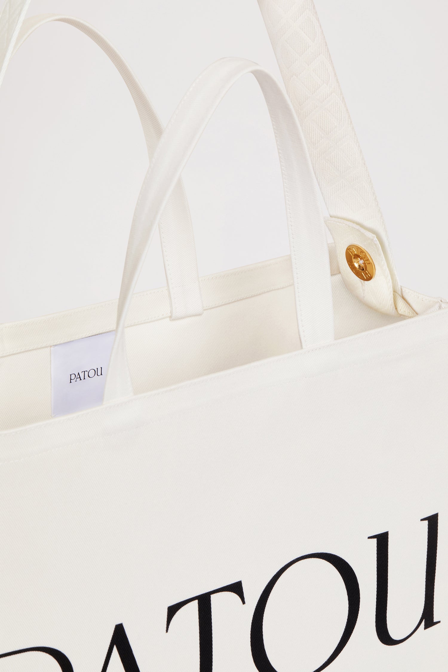 Patou - Patou canvas tote in organic cotton - Cream - Carry your Patou everywhere with you. Cream organic cotton tote. Patou lettering logo and JP monogram in black. White embossed shoulder strap with gold buttons. Two top handles. Can be carried by hand or on the shoulder.