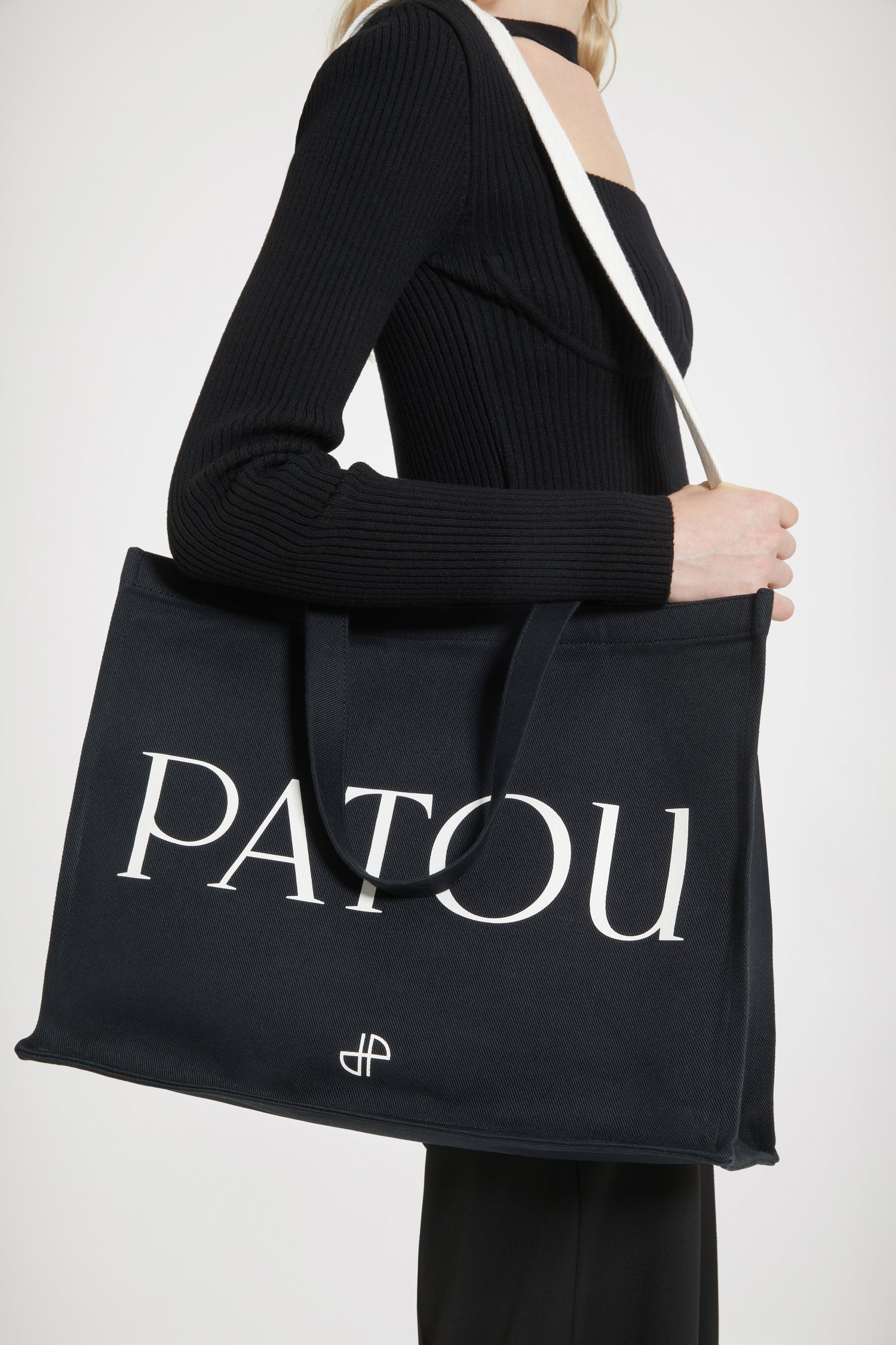 Patou - Patou canvas tote in organic cotton - Black - Carry your Patou everywhere with you. Black organic cotton tote. Patou lettering logo and JP monogram in white. White embossed shoulder strap with gold buttons. Two top handles. Can be carried by hand or on the shoulder.
