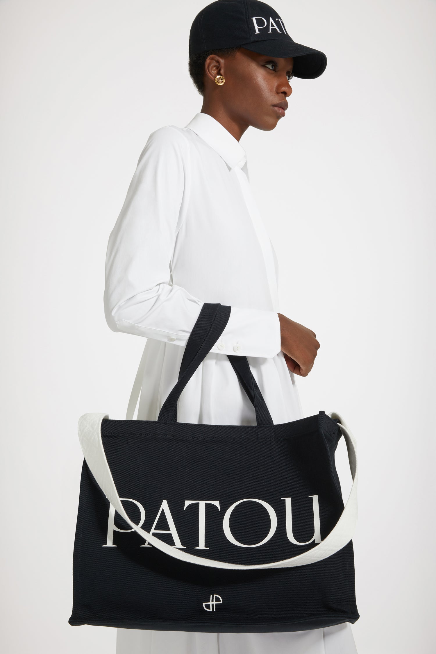 Patou - Patou canvas tote in organic cotton - Black - Carry your Patou everywhere with you. Black organic cotton tote. Patou lettering logo and JP monogram in white. White embossed shoulder strap with gold buttons. Two top handles. Can be carried by hand or on the shoulder.