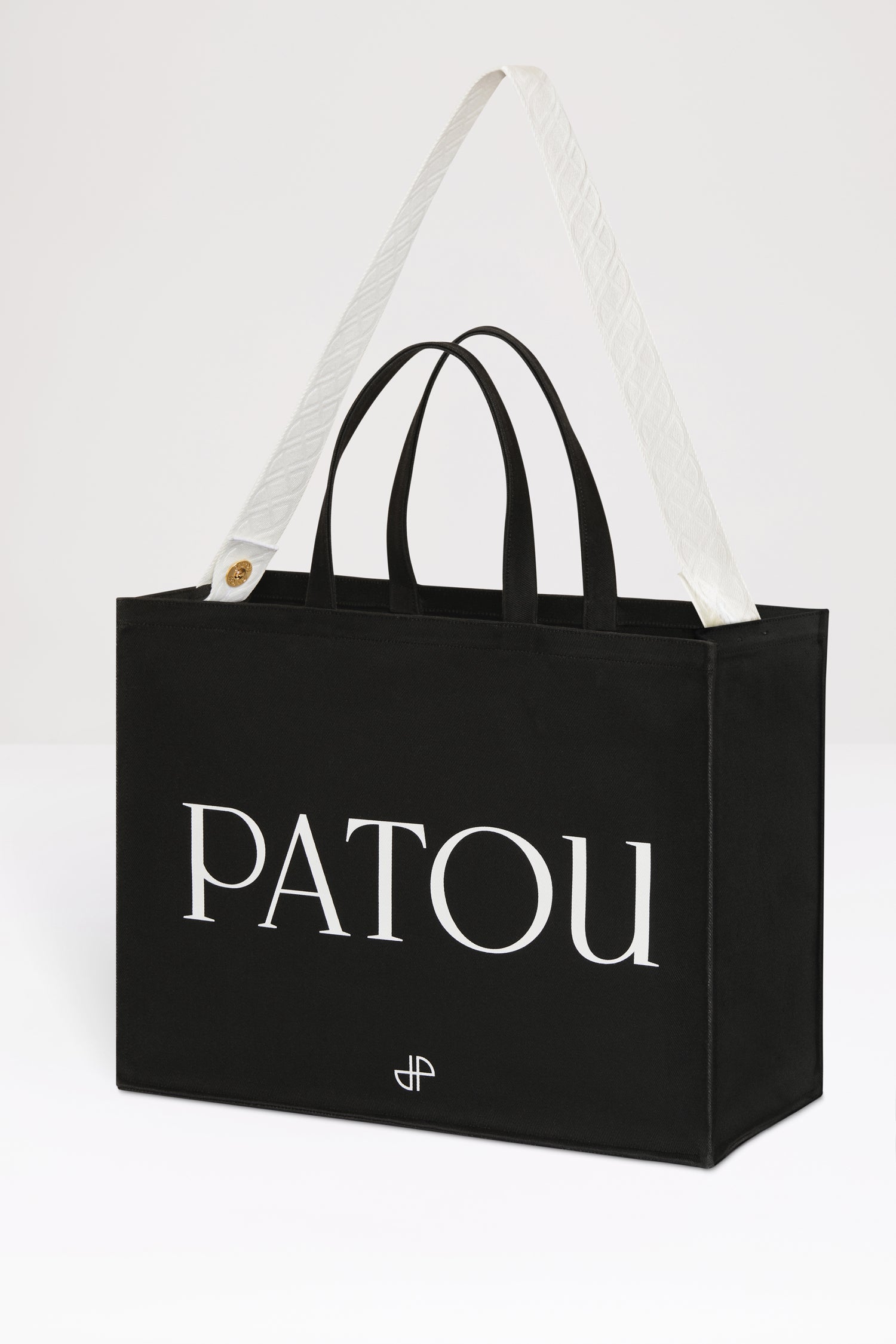 Patou - Patou canvas tote in organic cotton - Black - Carry your Patou everywhere with you. Black organic cotton tote. Patou lettering logo and JP monogram in white. White embossed shoulder strap with gold buttons. Two top handles. Can be carried by hand or on the shoulder.
