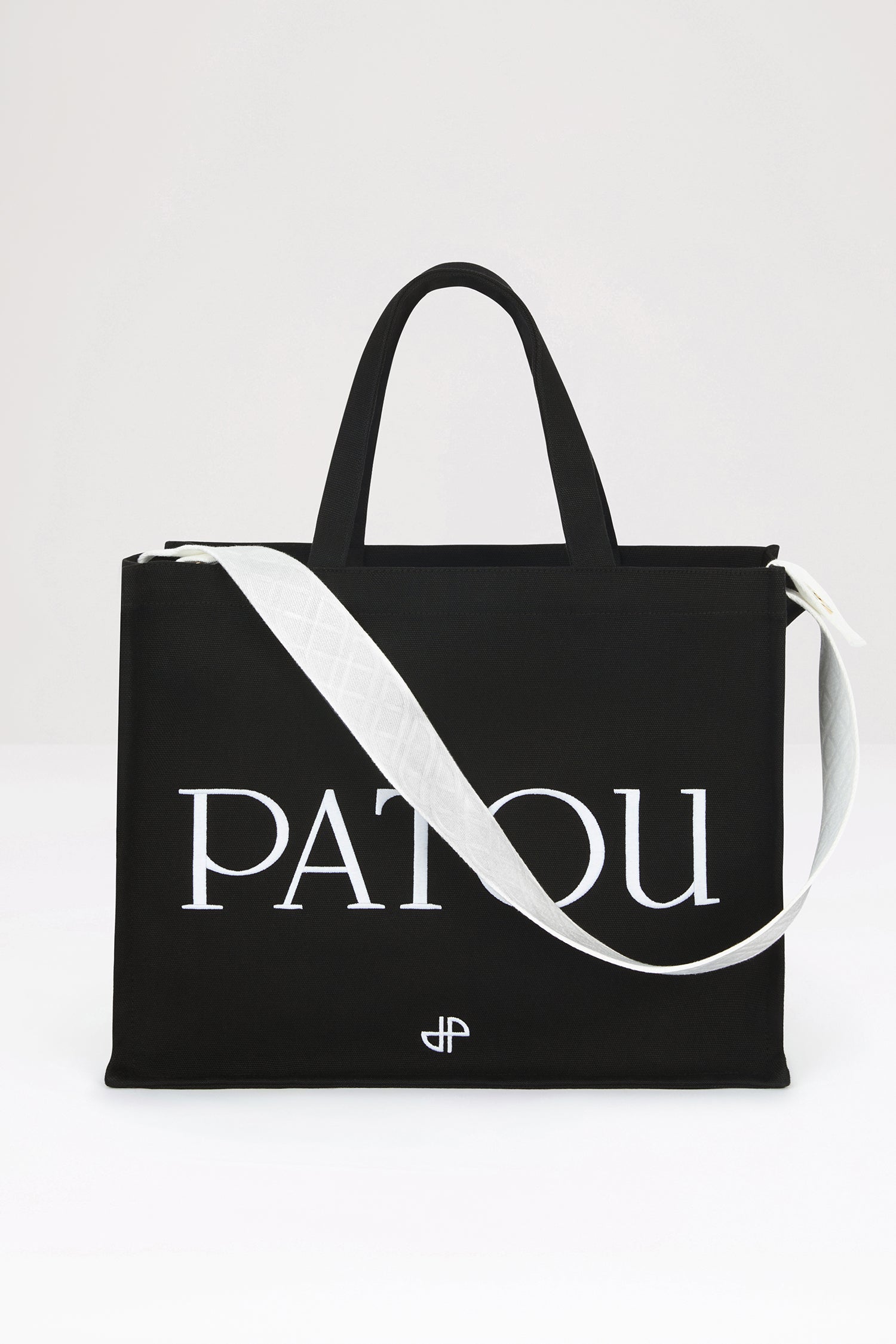 Patou - Patou canvas tote in organic cotton - Black - Carry your Patou everywhere with you. Black organic cotton tote. Patou lettering logo and JP monogram in white. White embossed shoulder strap with gold buttons. Two top handles. Can be carried by hand or on the shoulder.