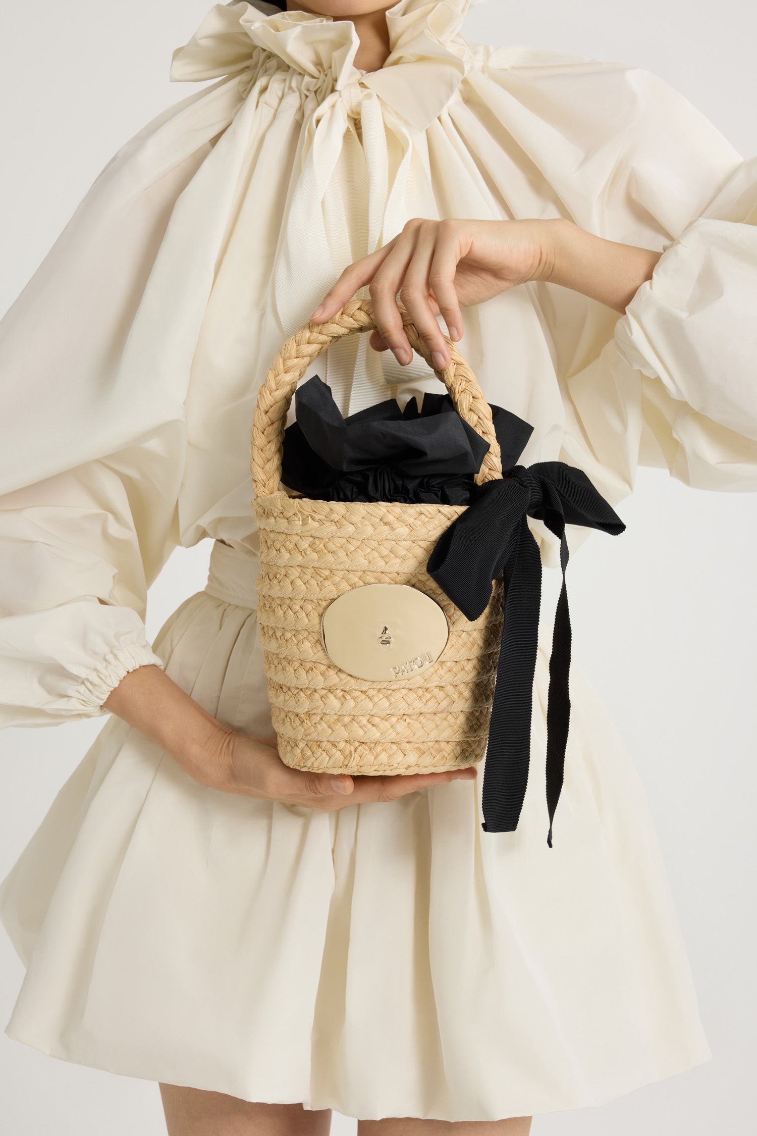 Patou - Panier seau en raphia - Vanilla - Panier en raphia couleur vanille. Forme seau avec anse tressée. Décoration dorée inspirée par la "Bocca della Verità". Doublure en tissu avec volant et noeud.