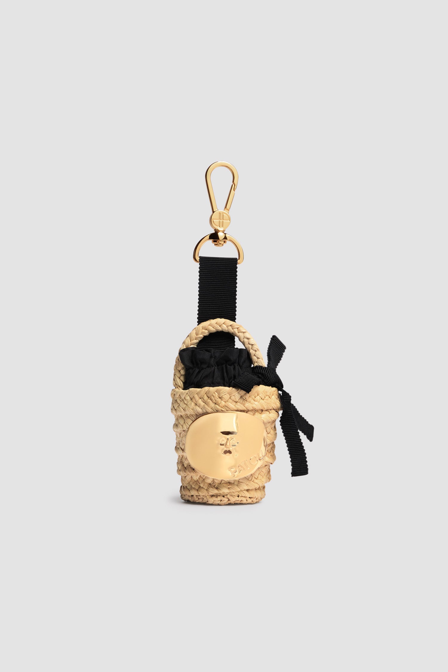 Patou - Iconic bucket charm in raffia - Vanilla - Vanilla natural raffia bucket charm. Gold-tone JP monogram-engraved hook fastening attached to a grosgrain bow with metal tips. Gold-tone embellishment inspired by the "Bocca della Verità" with engraved Patou logo. Black fabric lining with ruffle and bow.