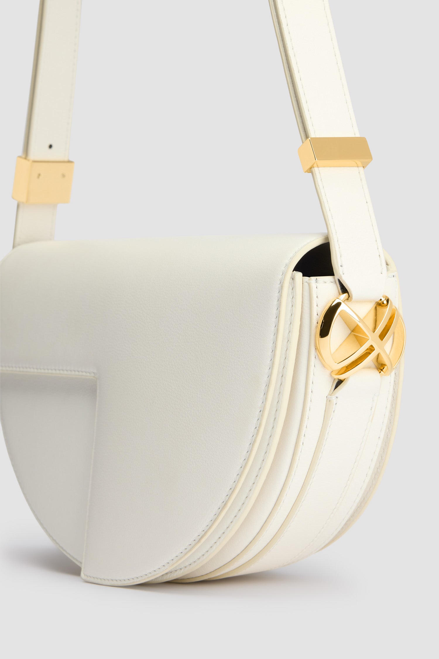 Patou - レザー製 Le Patou バッグ - Angora - アンゴラオフホワイトのレザー製ハンドバッグ。JPモノグラムにインスピレーションを得た幾何学的なカットアウトをあしらった半円形のフォルム。サイドにゴールドトーンのメタルパーツとJPモノグラム ディテール。調整可能なストラップで、ショルダーバッグ、クロスボディバッグ、ハンドバッグとしてお使いいただけます。ゴールドトーンのJPディテールをあしらったマグネットクロージャー。内部に複数のコンパートメント。エコライニング。長さ: 長さ: 25cm、高さ: 15cm、幅: 6cm ストラップの長さは3段階で調節可能:47 cm (ショルダー)、36 cm (クロスボディ)、28 cm (ハンド)