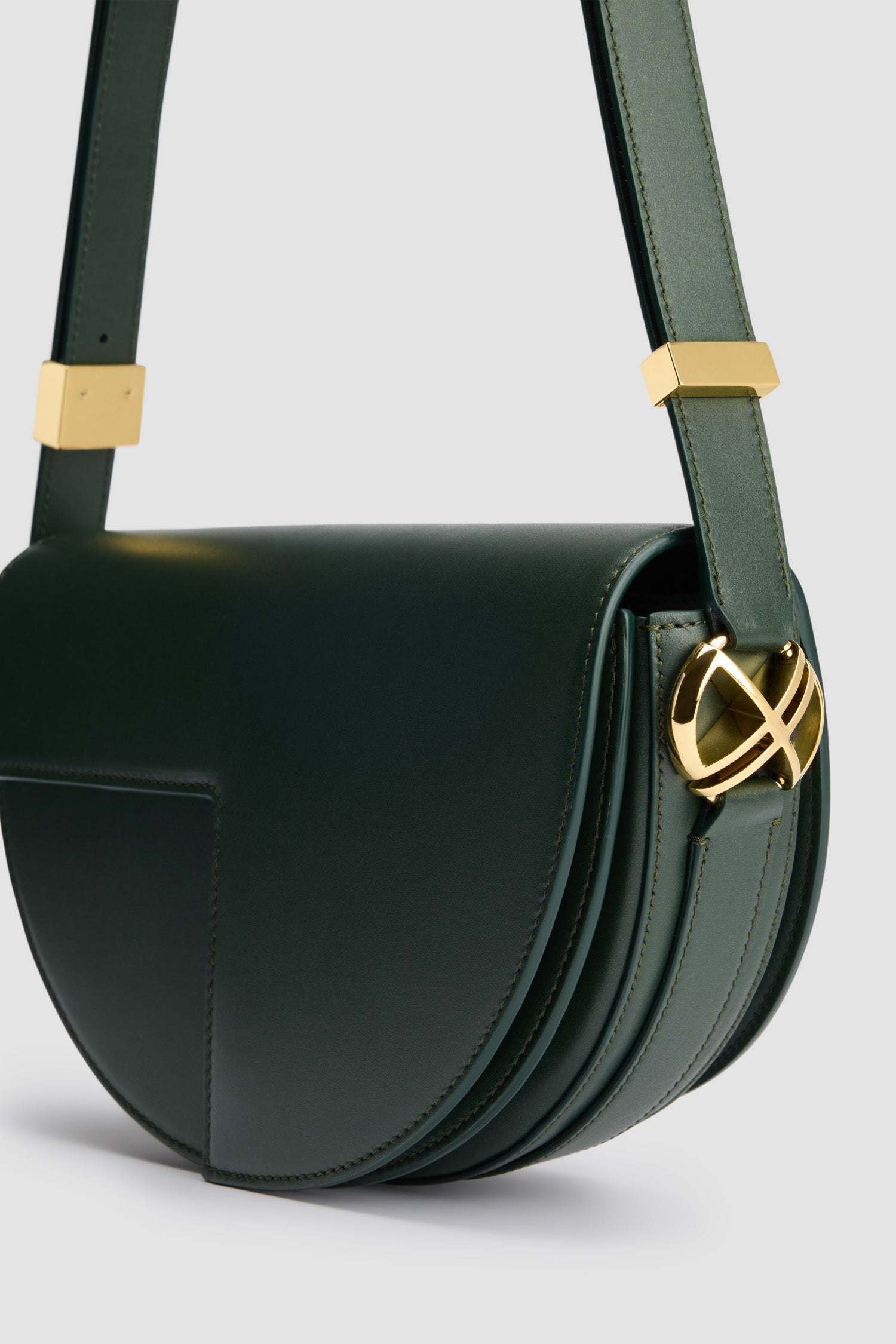 Patou - Le Patou - Bottle Green - Sac en cuir vert bouteille. Forme demi-lune avec découpes géométriques inspirée du monogramme JP. Pièces en métal doré avec détail JP inspiré d'une broche des archives Jean Patou. Bandoulière ajustable permettant un porté épaule, en bandoulière ou à la main. Fermeture aimantée avec détail JP doré. Compartiments multiples à l'intérieur.Dimensions : 25 cm de longueur, 15 cm de hauteur et 6 cm de profondeurBandoulière ajustable en 3 longueurs : 47 cm (sur l'épaule), 36 cm (en bandoulière), 28 cm (porté à la main)