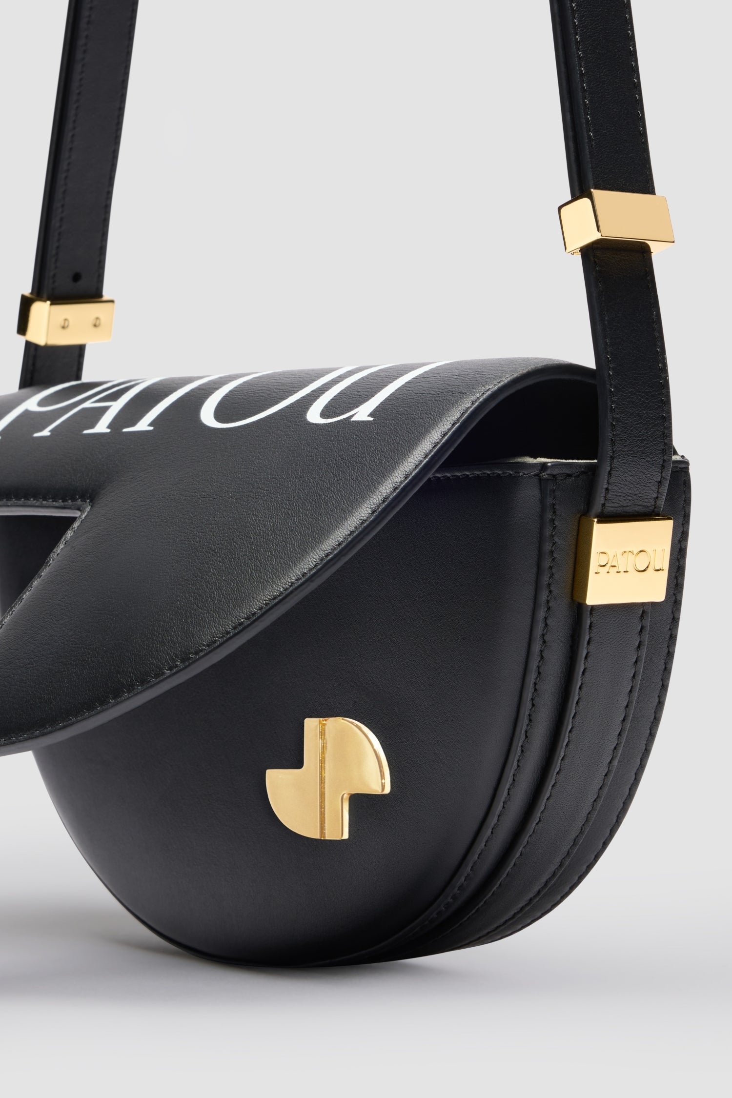 Patou - レザー製 Le Petit Patou ロゴバッグ - Black and White - ブラックのレザー製ハンドバッグ。JPモノグラムにインスピレーションを得た幾何学的なカットアウトをあしらった半円形のフォルム。サイドにゴールドトーンのメタルパーツとパトゥ刻印入りディテール。調整可能なストラップで、ショルダーバッグ、クロスボディバッグ、ハンドバッグとしてお使いいただけます。ゴールドトーンのJPディテールをあしらったマグネットクロージャー。内側のコンパートメント。エコライニング。サイズ: 横:20 cm 高さ:13 cm 幅:5 cm