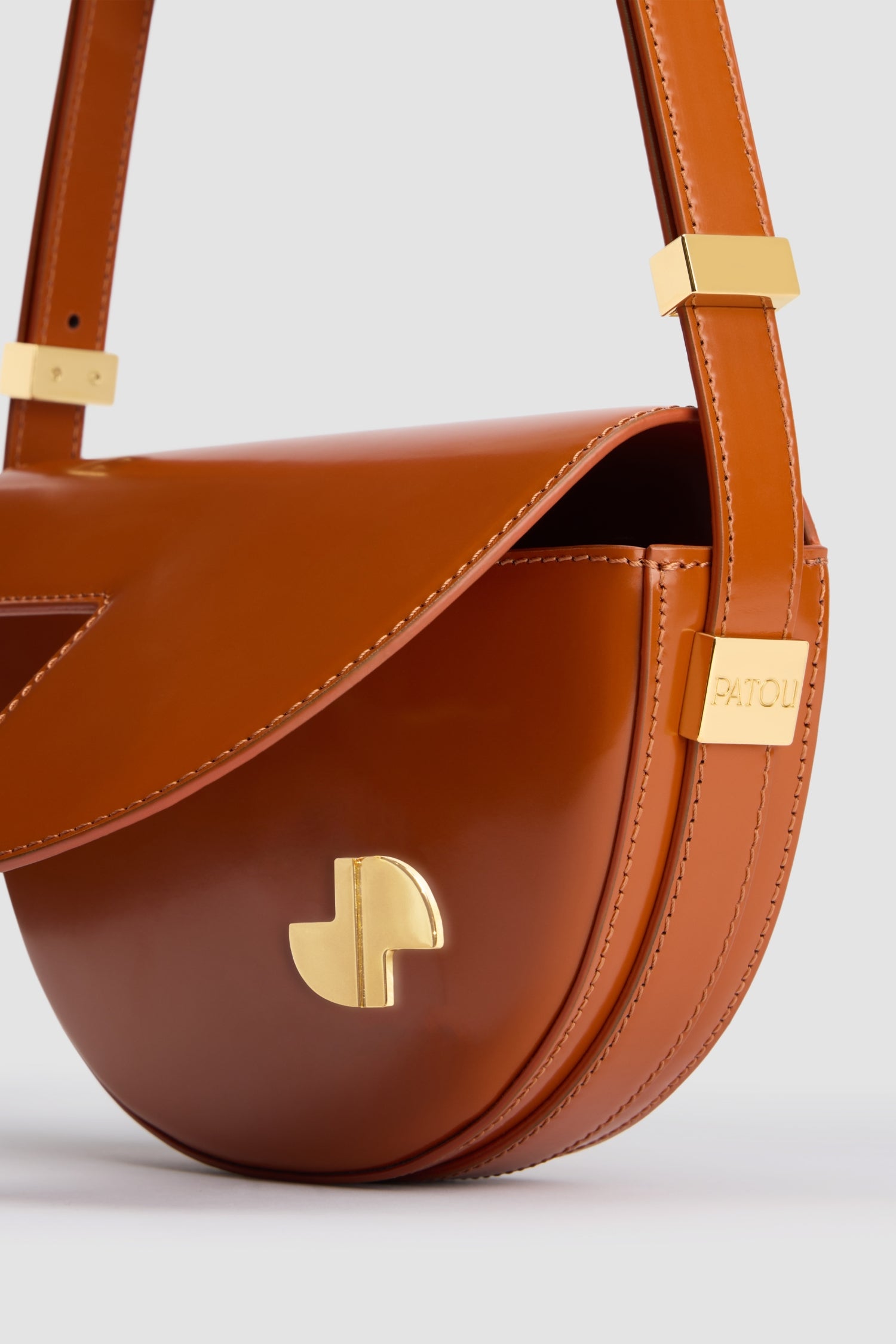 Patou - Le Petit Patou - Autumn Leaf - Sac en cuir marron feuille d'automne. Forme demi-lune avec découpes géométriques inspirée du monogramme JP. Pièce métallique gravée Patou sur le côté. Bandoulière ajustable permettant un porté épaule, en bandoulière ou à la main. Fermeture aimantée avec détail JP doré. Doublure éco-friendly.Dimensions : 20 cm de longueur, 13 cm de hauteur et 5 cm de profondeur.