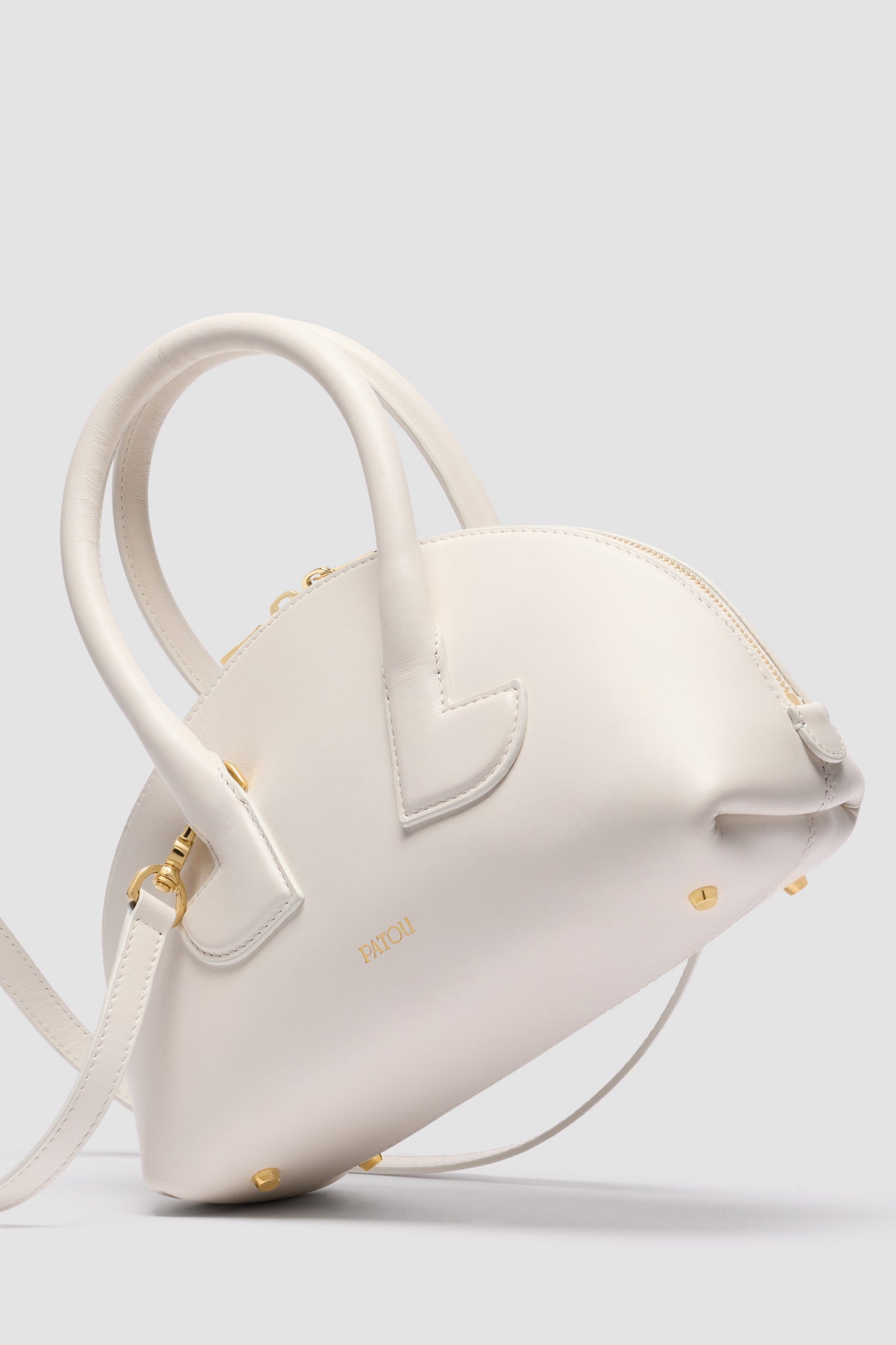 Patou - Le Patou Bowlingtasche aus Leder - White - Weiße Handtasche aus Glattleder. Bowlingform. Zwei Henkel mit geometrischen Ausschnitten. Abnehmbarer Schulterriemen. Goldfarbener Zwei-Wege-Reißverschluss. Goldfarbenes, eingeprägtes Patou Logo vorne. Füße aus goldfarbenem Metall.