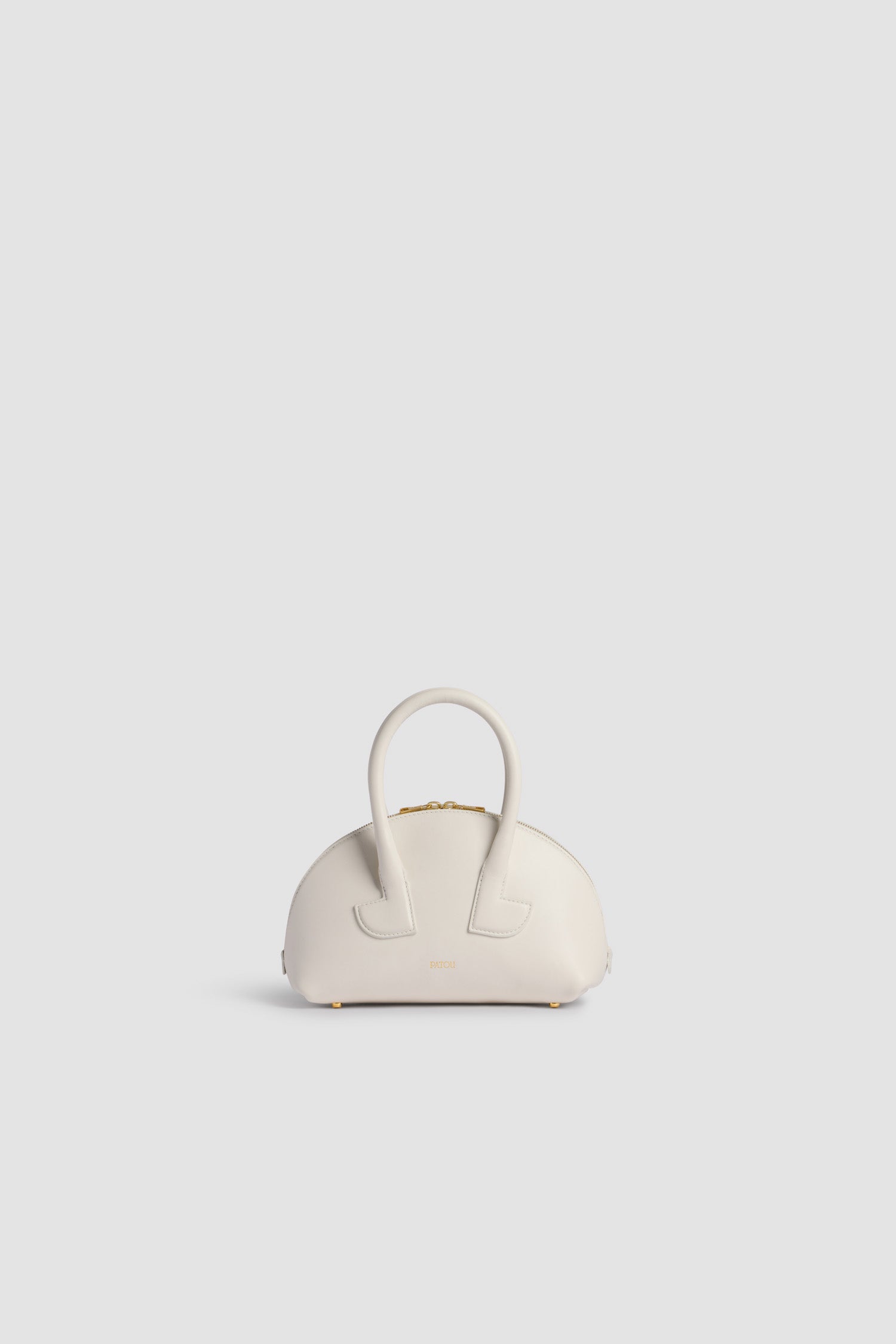 Patou - Le Patou Bowlingtasche aus Leder - White - Weiße Handtasche aus Glattleder. Bowlingform. Zwei Henkel mit geometrischen Ausschnitten. Abnehmbarer Schulterriemen. Goldfarbener Zwei-Wege-Reißverschluss. Goldfarbenes, eingeprägtes Patou Logo vorne. Füße aus goldfarbenem Metall.
