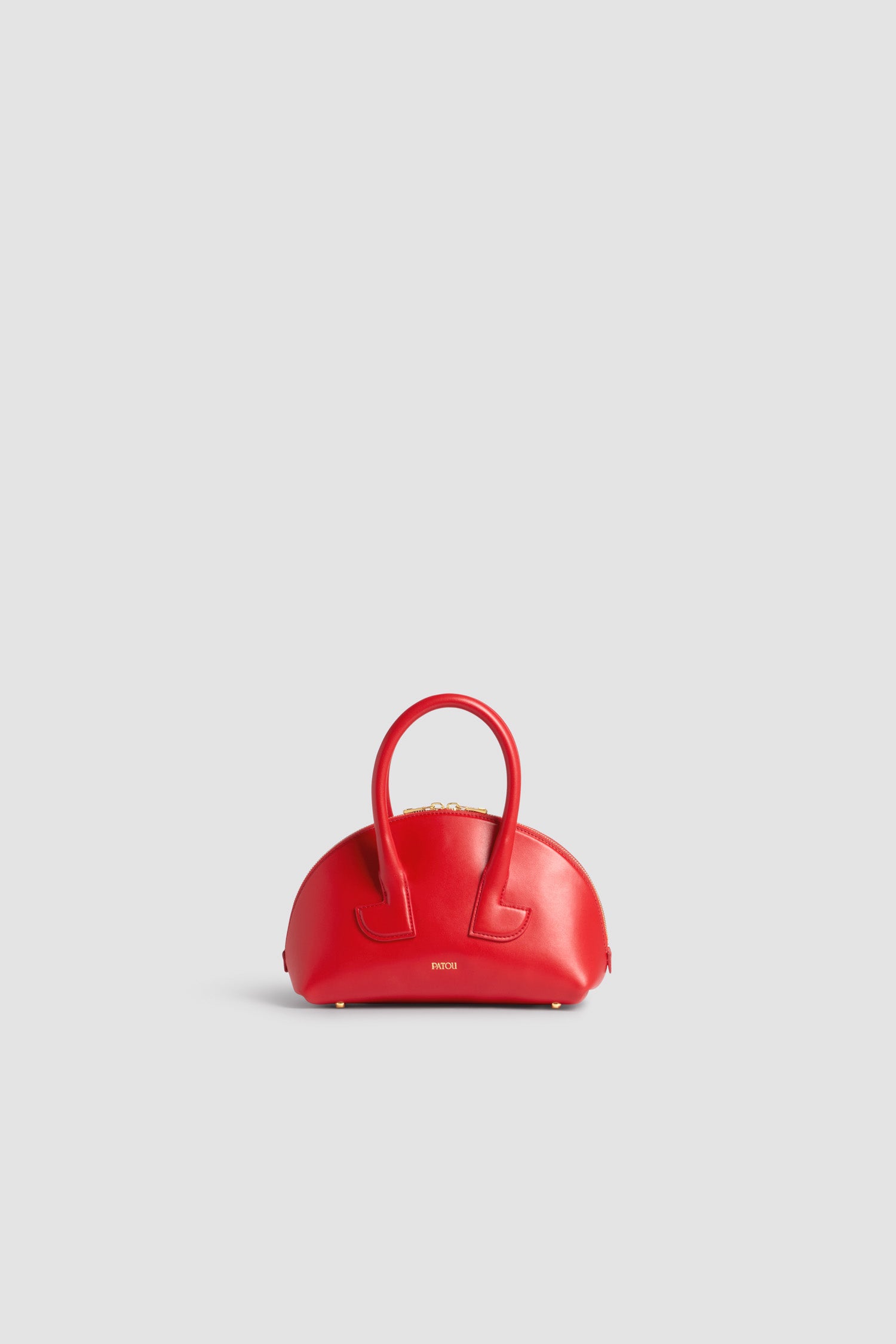 Patou - Le Patou Bowling en cuir - Lipstick Red - Sac en cuir lisse couleur rouge à lèvres. Forme bowling. Deux anses avec détails de découpes géométriques. Bandoulière amovible. Fermeture par zip doré à double curseur. Logo Patou doré sur le devant. Pieds en métal doré.