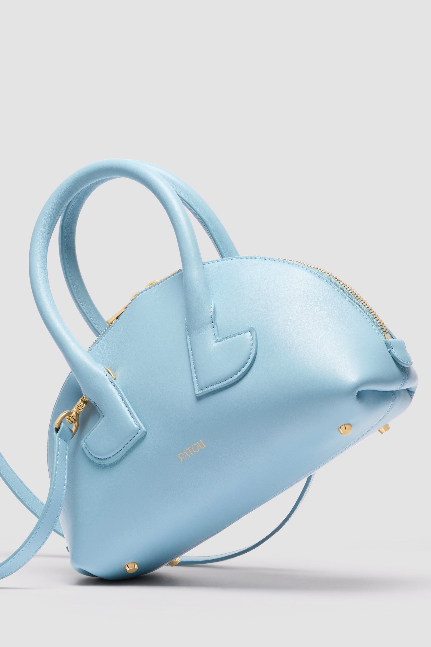 Patou - Le Patou Bowlingtasche aus Leder - Skylight Blue - Himmelblaue Handtasche aus Glattleder. Bowlingform. Zwei Henkel mit geometrischen Ausschnitten. Abnehmbarer Schulterriemen. Goldfarbener Zwei-Wege-Reißverschluss. Goldfarbenes, eingeprägtes Patou Logo vorne. Füße aus goldfarbenem Metall.