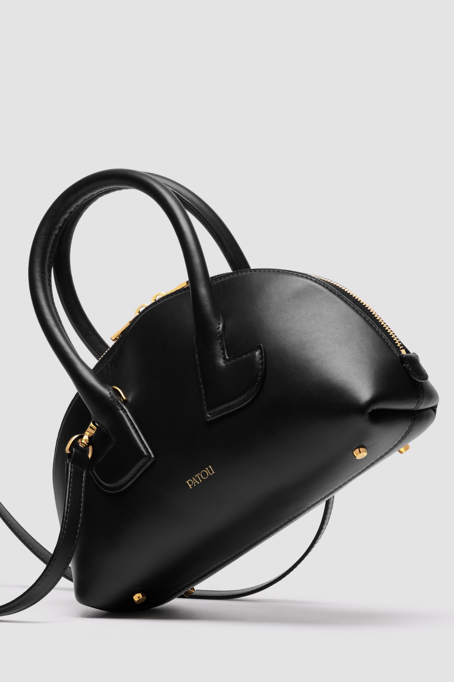 Patou - レザー製 Le Patou ボウリングバッグ - Black - ブラックのスムースレザー製ハンドバッグ。ボウリングシェイプ。ジオメトリックなカットアウトディテール入りのトップハンドル 2本。取り外し可能なショルダーストラップ。2Wayのゴールドトーン トップファスナー。前面にゴールドのエンボス入りパトゥロゴ。ゴールドトーンメタルの底鋲。