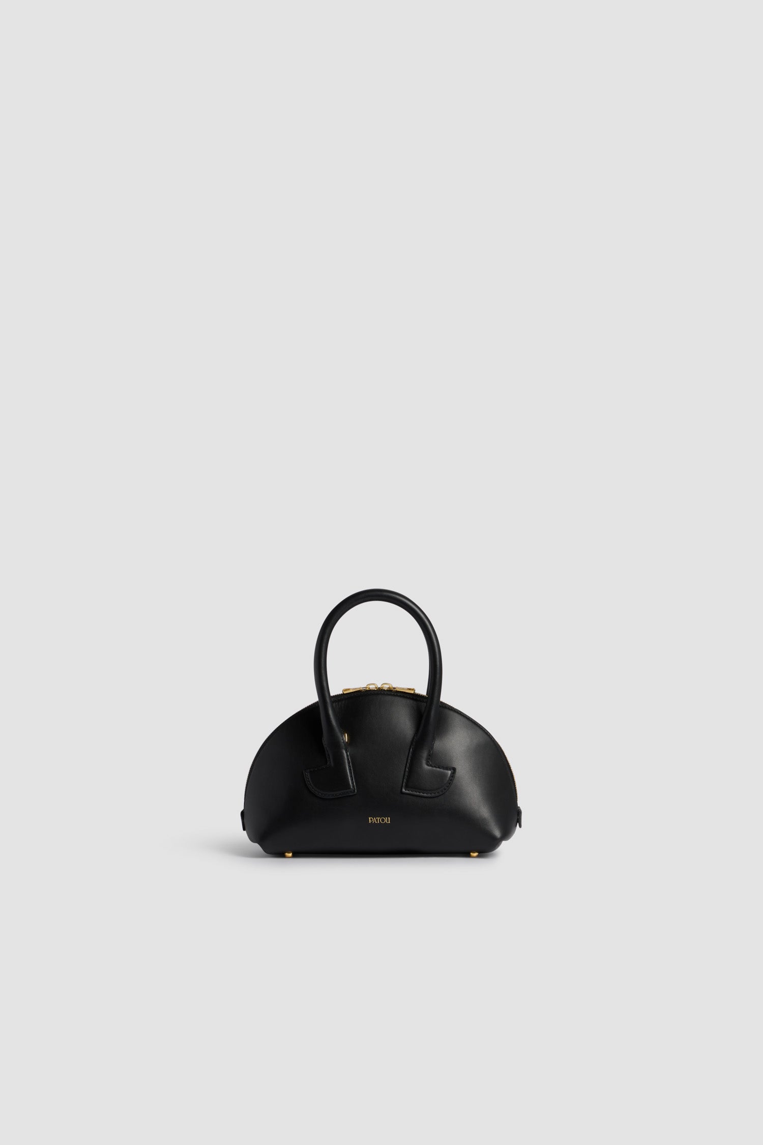 Patou - レザー製 Le Patou ボウリングバッグ - Black - ブラックのスムースレザー製ハンドバッグ。ボウリングシェイプ。ジオメトリックなカットアウトディテール入りのトップハンドル 2本。取り外し可能なショルダーストラップ。2Wayのゴールドトーン トップファスナー。前面にゴールドのエンボス入りパトゥロゴ。ゴールドトーンメタルの底鋲。
