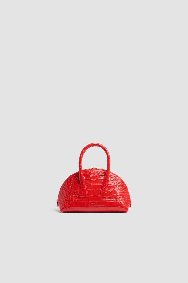 Patou - Borsa Le Patou Bowling in pelle di coccodrillo goffrata - Babylone Red - Borsa in pelle di coccodrillo goffrata Babylone Red. Forma bowling. Doppio manico con dettagli geometrici. Tracolla rimovibile. Chiusura con zip oro a doppio cursore. Logo Patou oro goffrato sul davanti. Piedini in metallo oro.