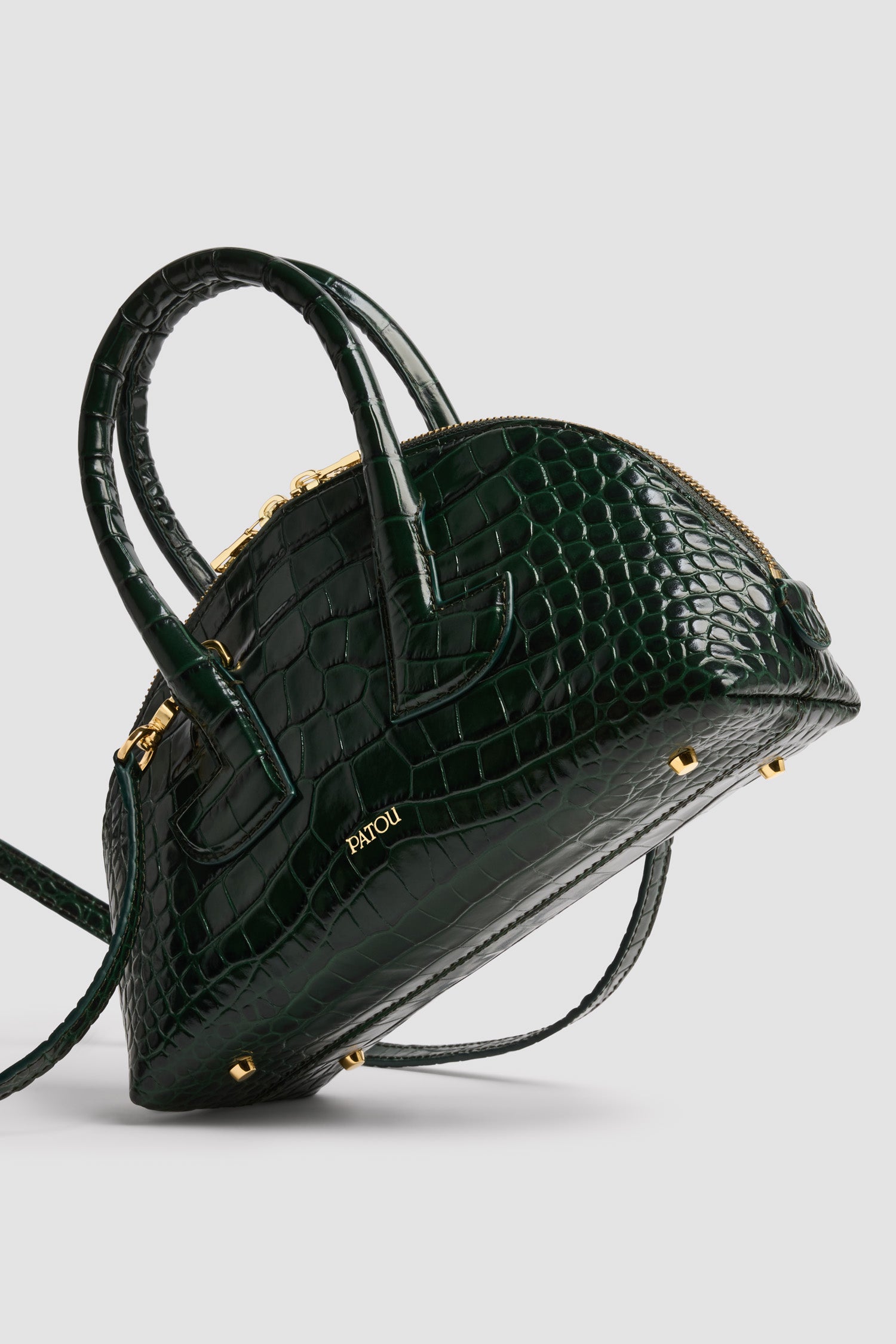 Patou - Le Patou クロコエンボスレザー ボウリングバッグ - Garden Green - ガーデングリーンのクロコ型押しレザーハンドバッグ。ボーリングシェイプ。ジオメトリックなカットアウトディテール入りのトップハンドル 2本。取り外し可能なショルダーストラップ。2Wayのゴールドトーン トップファスナー。前面にゴールドのエンボス入りパトゥロゴ。ゴールドトーンメタルの底鋲。