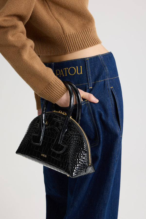 Patou - Sac Le Patou Bowling en cuir embossé crocodile - Black - Sac à main en cuir embossé crocodile noir. Forme bowling. Deux anses avec détails de découpes géométriques. Bandoulière amovible. Fermeture par zip doré à double curseur. Logo Patou doré embossé sur le devant. Pieds en métal doré.