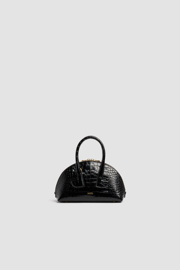 Patou - Sac Le Patou Bowling en cuir embossé crocodile - Black - Sac à main en cuir embossé crocodile noir. Forme bowling. Deux anses avec détails de découpes géométriques. Bandoulière amovible. Fermeture par zip doré à double curseur. Logo Patou doré embossé sur le devant. Pieds en métal doré.