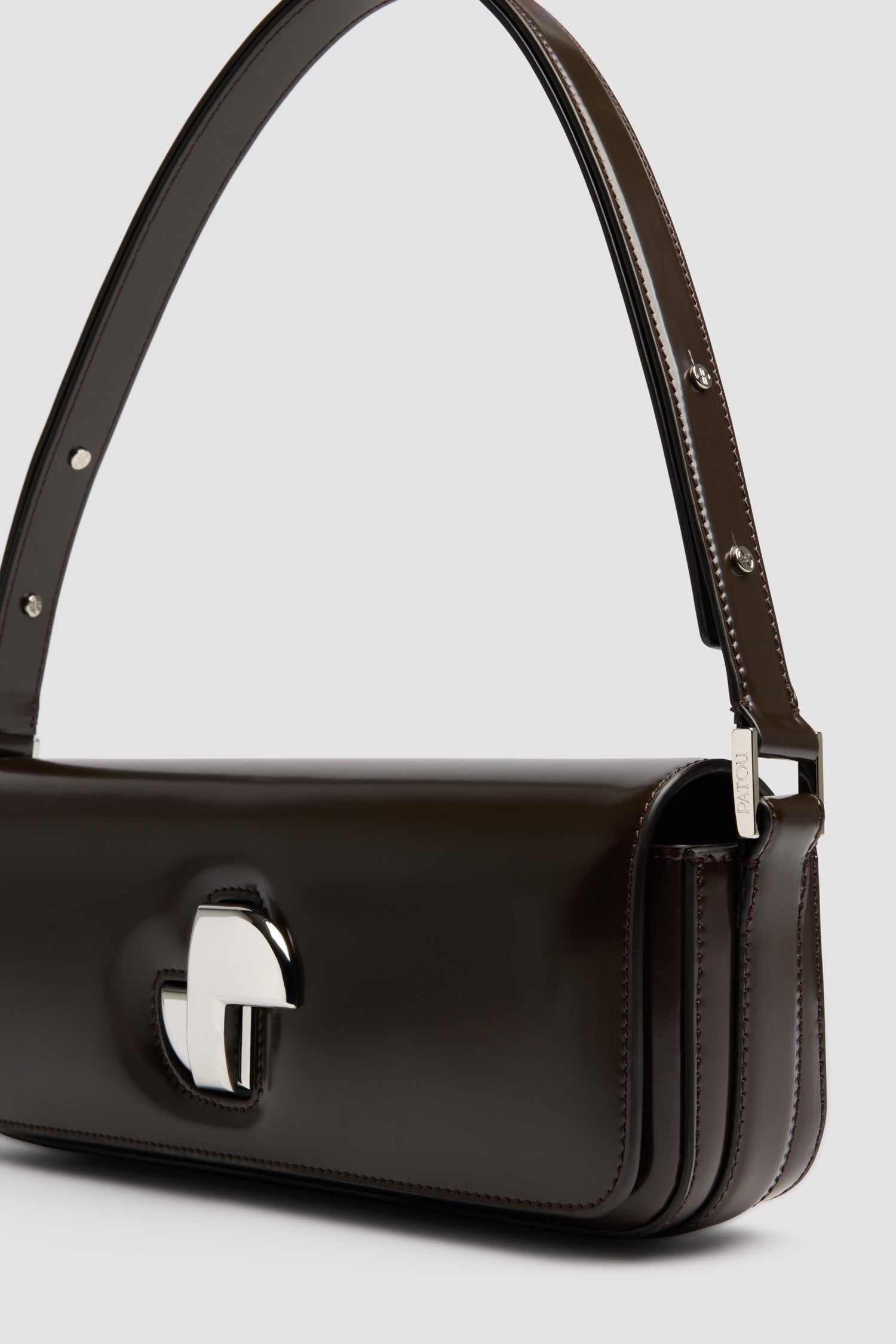 Patou - Sac Le Lock Baguette en cuir - Smoked Ebony - Sac à main en cuir brillant couleur ébène fumé. Sac de jour classique revisité avec une forme allongée. Fermoir rotatif JP doré d’inspiration Art Déco sur le devant. Bandoulière réglable pouvant être portée courte ou longue. Doublure en cuir.