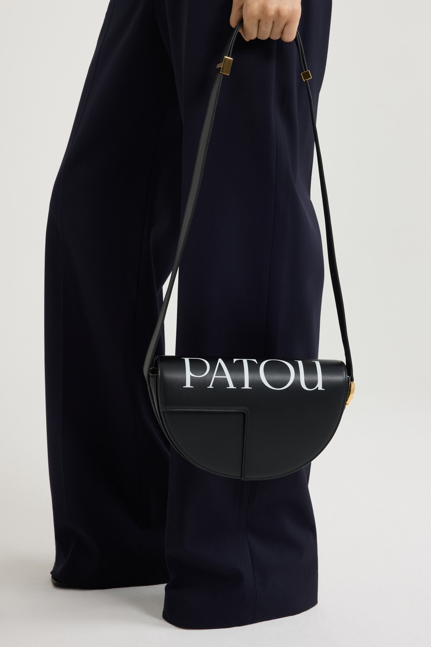 Patou - Le Patou bag in leather - Black and White - Black smooth leather handbag. White Patou logo printed across the top. Half-circle shape with geometric cut-outs inspired by the JP monogram. Gold-tone hardware with JP monogram detail at the side. Adjustable strap that allows it to be worn on the shoulder, across the body or carried by hand. Magnetic closure with gold-tone JP detail. Multiple compartments inside.Measures: 25 cm (length), 15 cm (height), 6 cm (depth)3 lengths for the adjustable strap: 47 cm (on the shoulder), 36 cm (across the body), 28 cm (carried by hand)