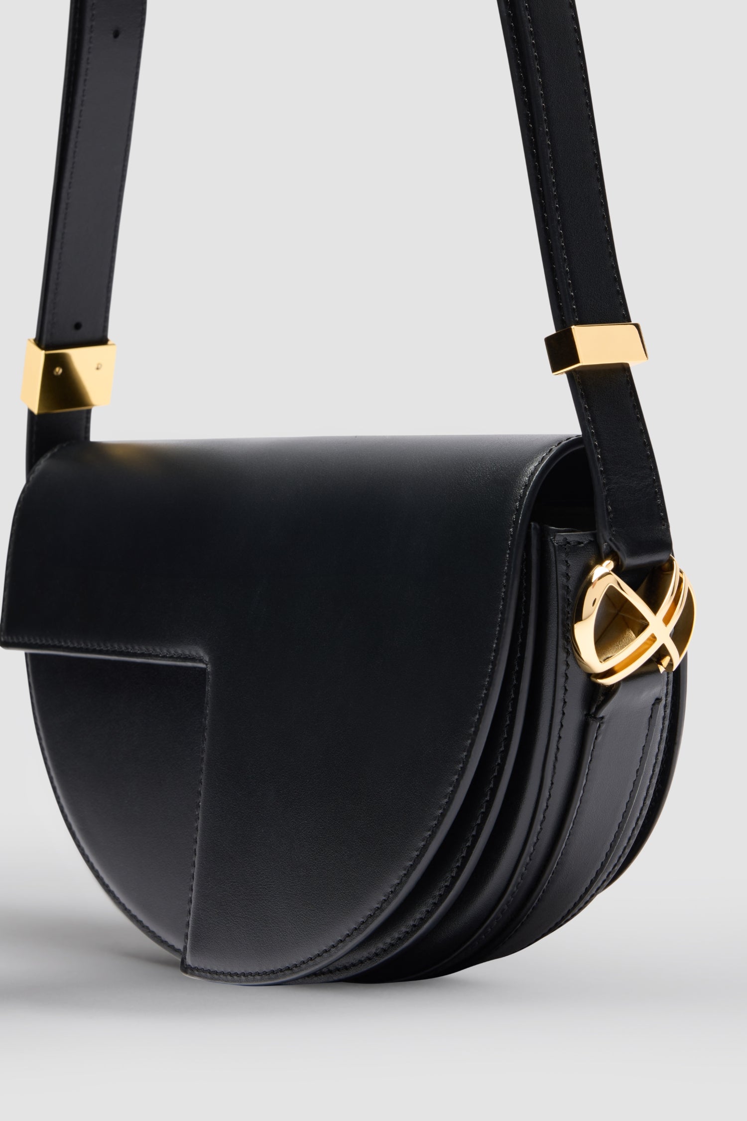 Patou - レザー製 Le Patou バッグ - Black - ブラックのスムースレザー製ハンドバッグ。JPモノグラムにインスピレーションを得た幾何学的なカットアウトをあしらった半円形のフォルム。サイドにゴールドトーンのメタルパーツとJPモノグラム ディテール。調整可能なストラップで、ショルダーバッグ、クロスボディバッグ、ハンドバッグとしてお使いいただけます。ゴールドトーンのJPディテールをあしらったマグネットクロージャー。内部に複数のコンパートメント。長さ: 長さ: 25cm、高さ: 15cm、幅: 6cmストラップの長さは3段階で調節可能:47 cm (ショルダー)、36 cm (クロスボディ)、28 cm (ハンド)