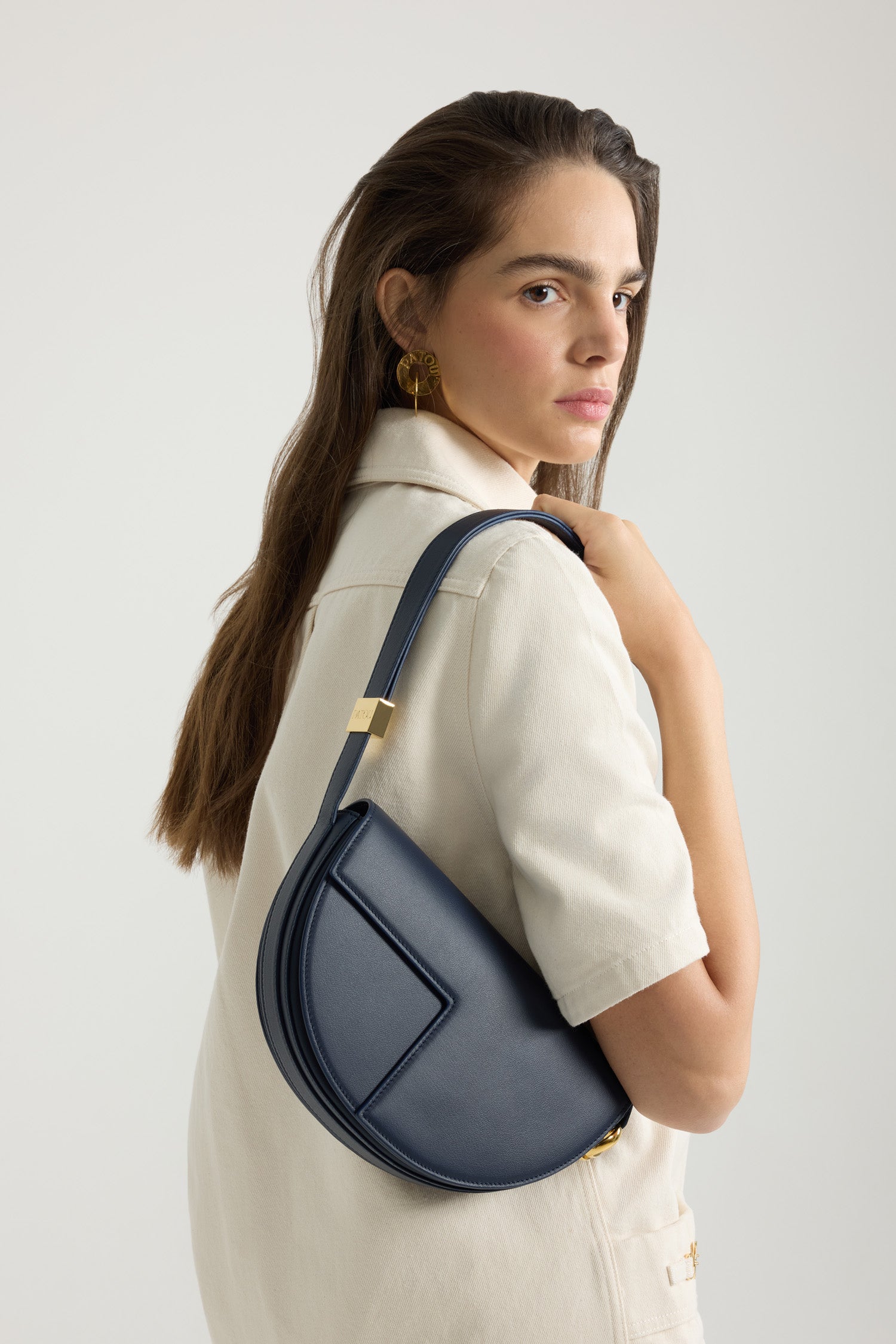 Patou - Le Patou - Navy Black - Sac en cuir noir marine brillant. Réalisé en cuir de grande qualité provenant de stocks dormants issus des surplus de production. Forme demi-lune avec découpes géométriques inspirée du monogramme JP. Pièces en métal doré avec détail JP inspiré d'une broche des archives Jean Patou. Bandoulière ajustable permettant un porté épaule, en bandoulière ou à la main. Fermeture aimantée avec détail JP doré. Compartiments multiples à l'intérieur.Dimensions : 25 cm de longueur, 15 cm de hauteur et 6 cm de profondeurBandoulière ajustable en 3 longueurs : 47 cm (sur l'épaule), 36 cm (en bandoulière), 28 cm (porté à la main)