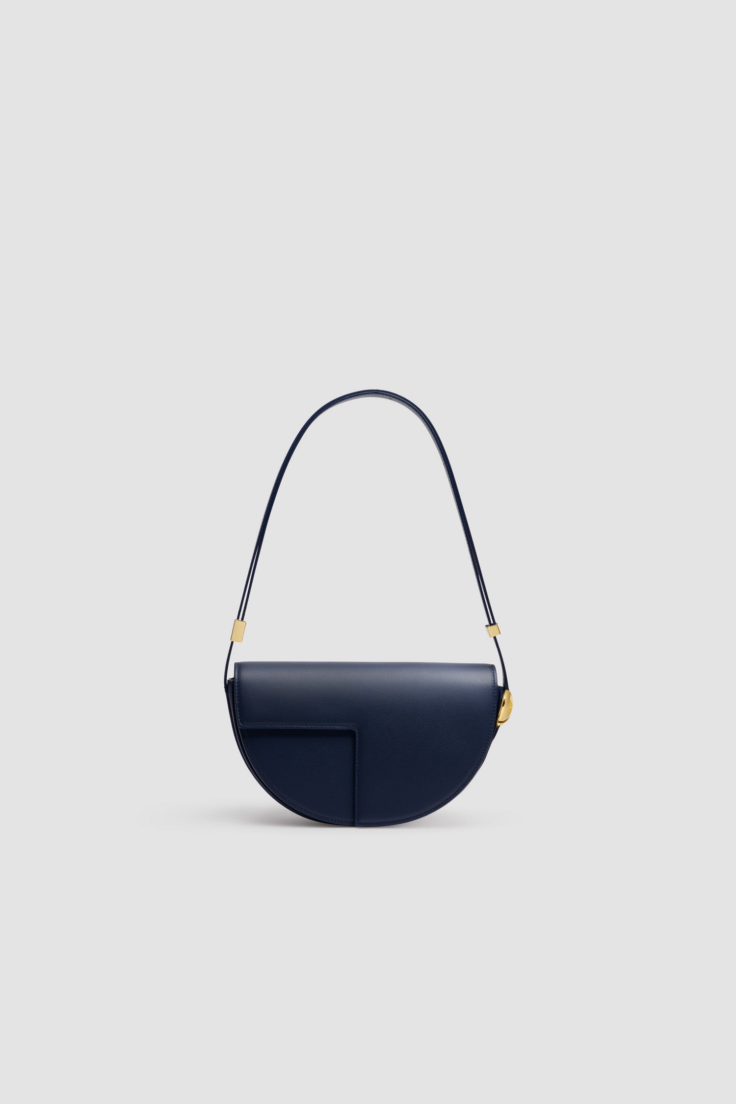 Patou - Le Patou - Navy Black - Sac en cuir noir marine brillant. Réalisé en cuir de grande qualité provenant de stocks dormants issus des surplus de production. Forme demi-lune avec découpes géométriques inspirée du monogramme JP. Pièces en métal doré avec détail JP inspiré d'une broche des archives Jean Patou. Bandoulière ajustable permettant un porté épaule, en bandoulière ou à la main. Fermeture aimantée avec détail JP doré. Compartiments multiples à l'intérieur.Dimensions : 25 cm de longueur, 15 cm de hauteur et 6 cm de profondeurBandoulière ajustable en 3 longueurs : 47 cm (sur l'épaule), 36 cm (en bandoulière), 28 cm (porté à la main)