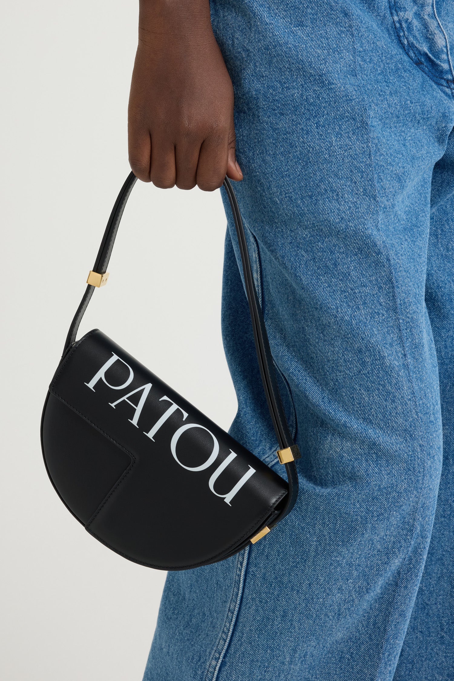 Patou - レザー製 Le Petit Patou ロゴバッグ - Black and White - ブラックのレザー製ハンドバッグ。JPモノグラムにインスピレーションを得た幾何学的なカットアウトをあしらった半円形のフォルム。サイドにゴールドトーンのメタルパーツとパトゥ刻印入りディテール。調整可能なストラップで、ショルダーバッグ、クロスボディバッグ、ハンドバッグとしてお使いいただけます。ゴールドトーンのJPディテールをあしらったマグネットクロージャー。内側のコンパートメント。エコライニング。サイズ: 横:20 cm 高さ:13 cm 幅:5 cm