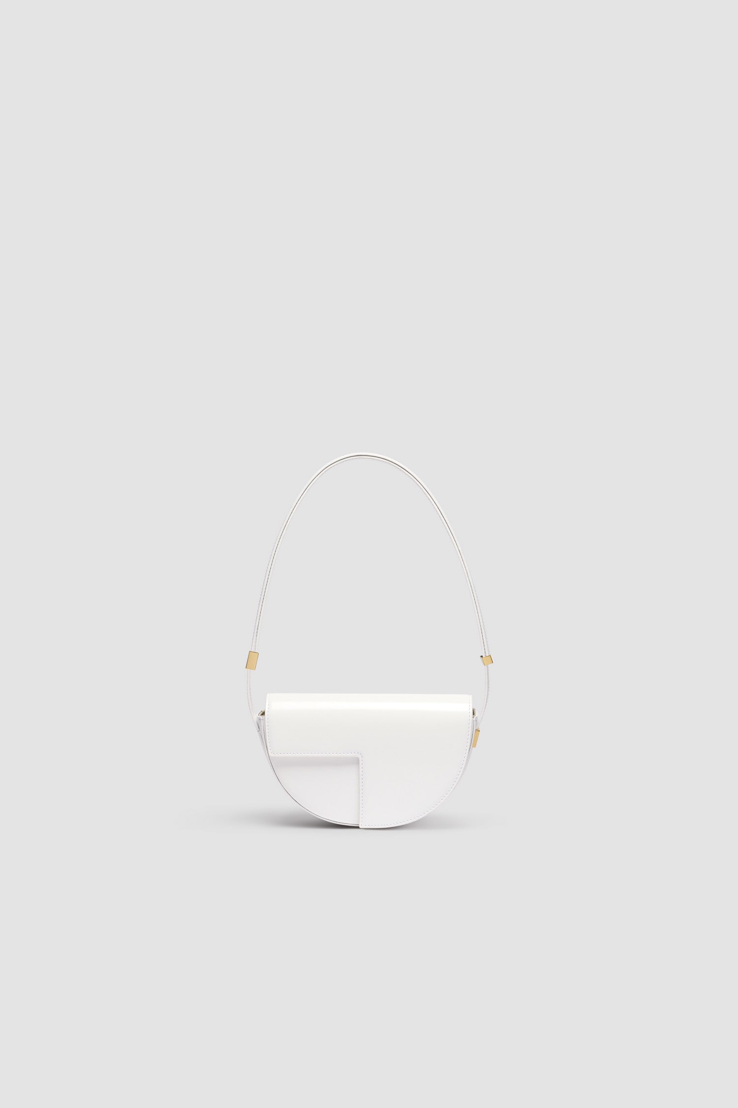 Patou - レザー製 Le Petit Patou バッグ - White - ホワイトのつややかなレザー製ハンドバッグ。JPモノグラムにインスピレーションを得た幾何学的なカットアウトをあしらった半円形のフォルム。サイドにゴールドトーンのメタルパーツとパトゥロゴ刻印入りディテール。調整可能なストラップで、ショルダーバッグ、クロスボディバッグ、ハンドバッグとしてお使いいただけます。ゴールドトーンのJPディテールをあしらったマグネットクロージャー。内側のコンパートメント。長さ: 20 cm 高さ:13 cm 幅:5 cm