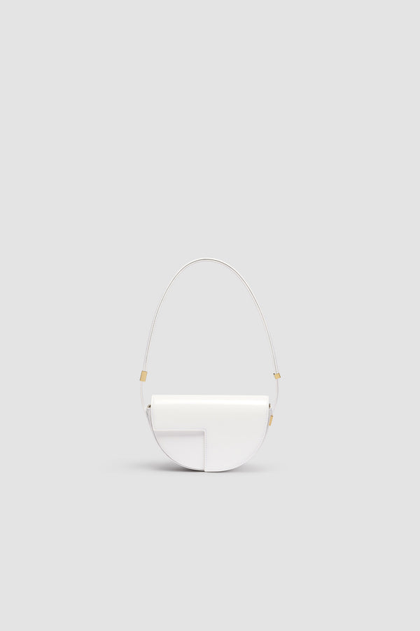 Patou - Le Petit Patou - White - Sac en cuir brillant blanc. Forme demi-lune avec découpes géométriques inspirée du monogramme JP. Pièce métallique gravée Patou sur le côté. Bandoulière ajustable permettant un porté épaule, en bandoulière ou à la main. Fermeture aimantée avec détail JP doré. Doublure éco-friendly.Dimensions : 20 cm de longueur, 13 cm de hauteur et 5 cm de profondeur.