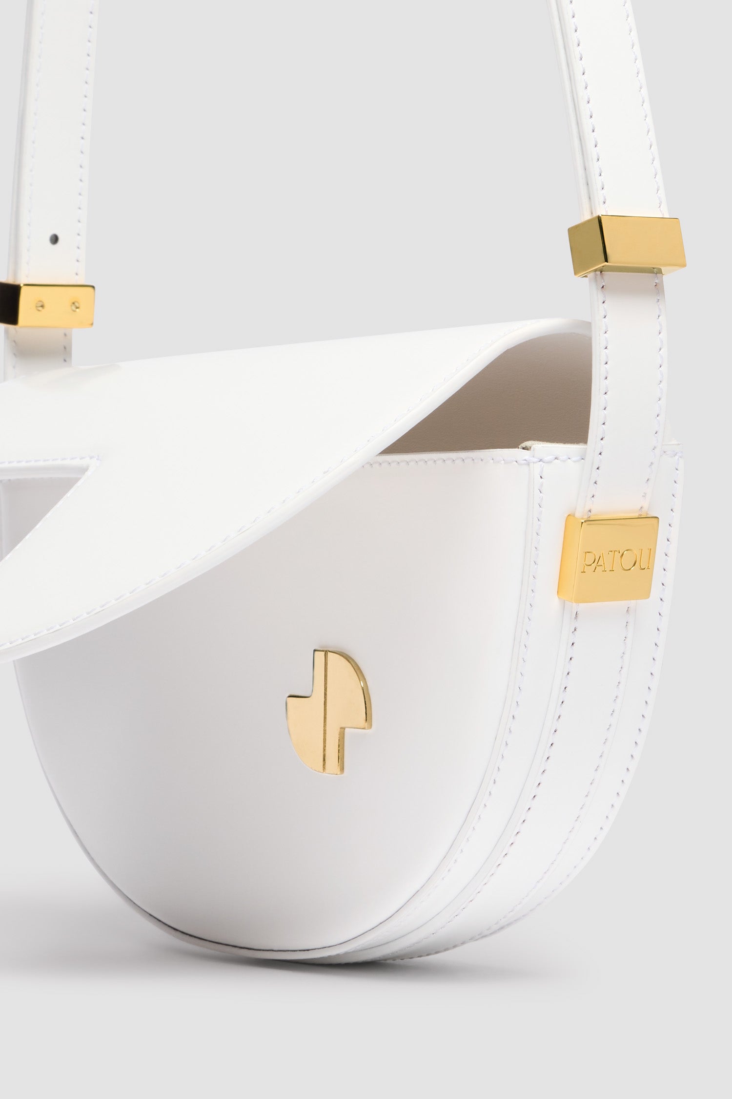 Patou - レザー製 Le Petit Patou バッグ - White - ホワイトのつややかなレザー製ハンドバッグ。JPモノグラムにインスピレーションを得た幾何学的なカットアウトをあしらった半円形のフォルム。サイドにゴールドトーンのメタルパーツとパトゥロゴ刻印入りディテール。調整可能なストラップで、ショルダーバッグ、クロスボディバッグ、ハンドバッグとしてお使いいただけます。ゴールドトーンのJPディテールをあしらったマグネットクロージャー。内側のコンパートメント。長さ: 20 cm 高さ:13 cm 幅:5 cm