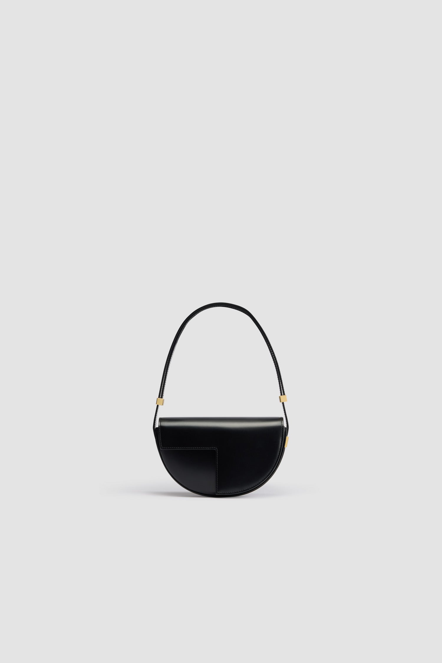 Patou - Le Petit Patou bag in leather - Black - Black leather handbag. Half-circle shape with geometric cut-outs inspired by the JP monogram. Gold-tone hardware with Patou-engraved detail at the side. Adjustable strap that allows it to be worn on the shoulder, across the body or carried by hand. Magnetic closure with gold-tone JP detail. Internal compartment. Eco lining.Measures: 20cm (length), 13cm (height), 5cm (depth)