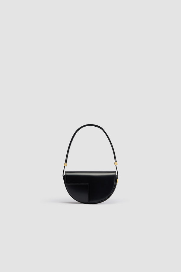 Patou - Le Petit Patou - Black - Sac en cuir noir. Forme demi-lune avec découpes géométriques inspirée du monogramme JP. Pièce métallique gravée Patou sur le côté. Bandoulière ajustable permettant un porté épaule, en bandoulière ou à la main. Fermeture aimantée avec détail JP doré. Doublure éco-responsable.Dimensions : 20 cm de longueur, 13 cm de hauteur et 5 cm de profondeur.
