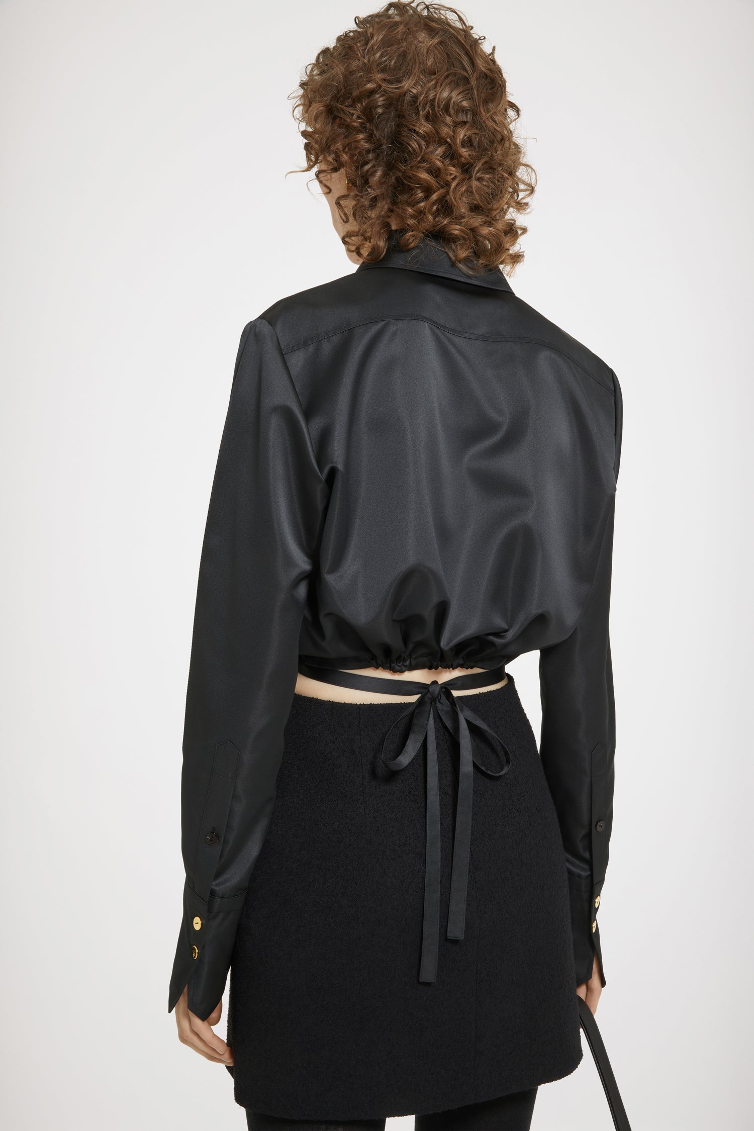 Patou - Camicia corta con ritagli in raso sostenibile - Black - Sinfonia in Patou maggiore.Camicia in raso di poliestere riciclato nero. Silhouette corta con ritagli a ispirazione violino ai lati. Bottoni nascosti. Cintura in vita con tunnel sul retro. Pieghe ai polsini. Polsini abbottonati.