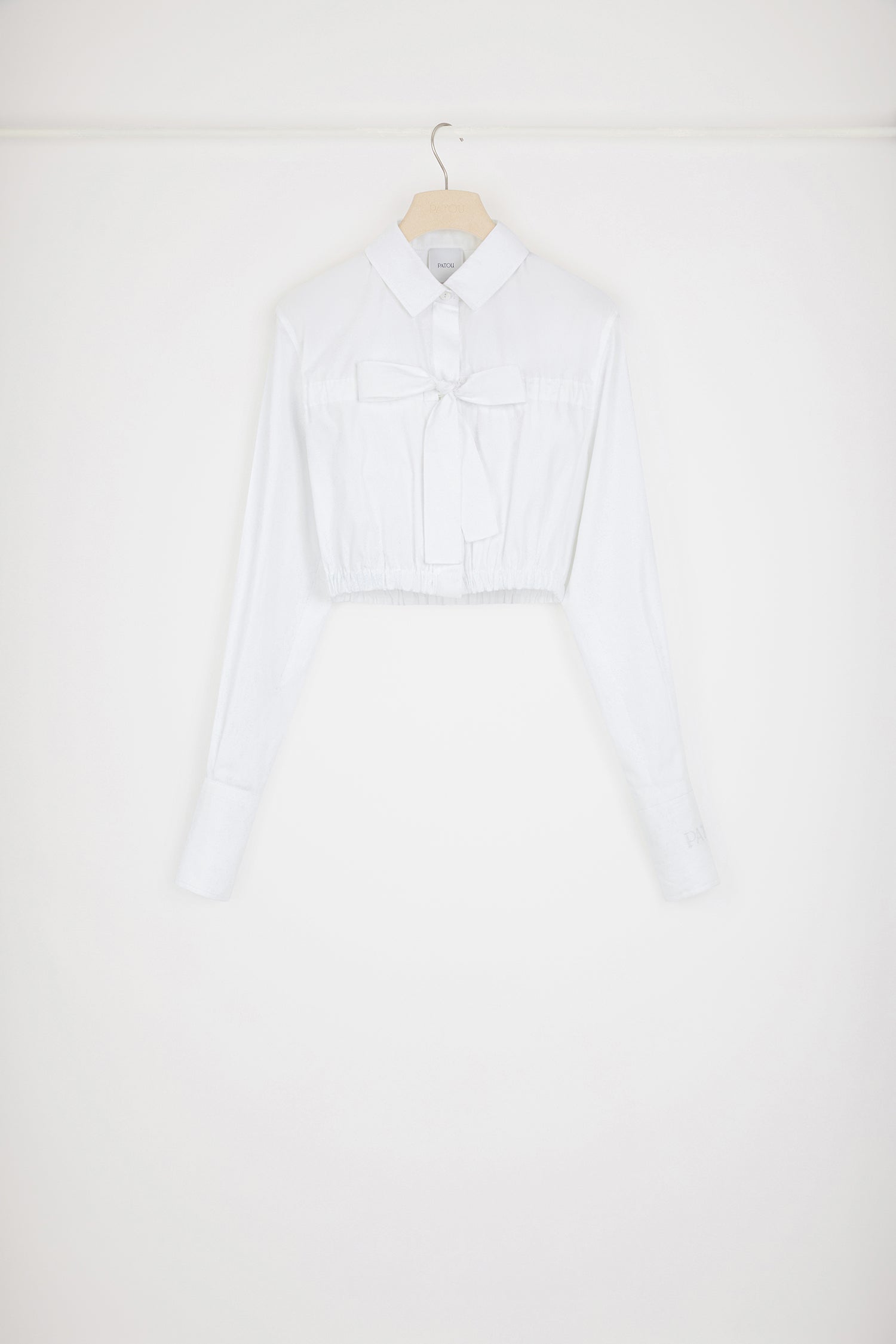 Patou - Camicia corta con fiocco in cotone ecosostenibile - White - Una camicia con i fiocchi.Camicia in popeline di cotone ecosostenibile bianca. Modello cropped e largo. Colletto classico. Fiocco al petto. Chiusura nascosta con bottoni incisi JP. Vita elasticizzata. Polsini abbottonati. Patou ricamato sulla manica sinistra.