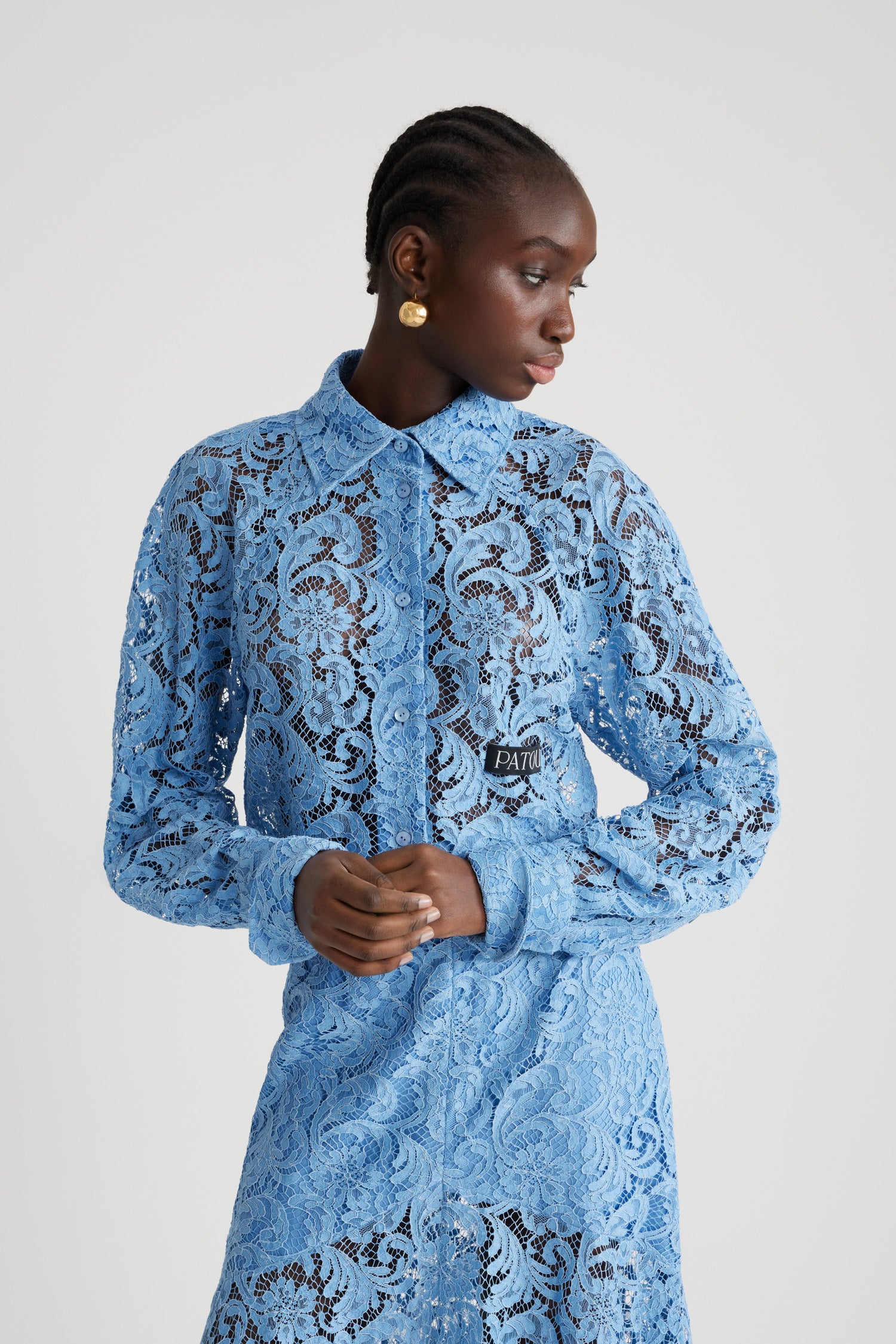 Patou - Chemise courte en dentelle de coton bio - Airy Blue - Chemise en dentelle de coton bio et viscose éco-responsable bleu ciel. Modèle court. Col de chemise. Boutons en nacre gravés JP. Étiquette Patou sur le devant. Manches raglan. Poignets boutonnés.