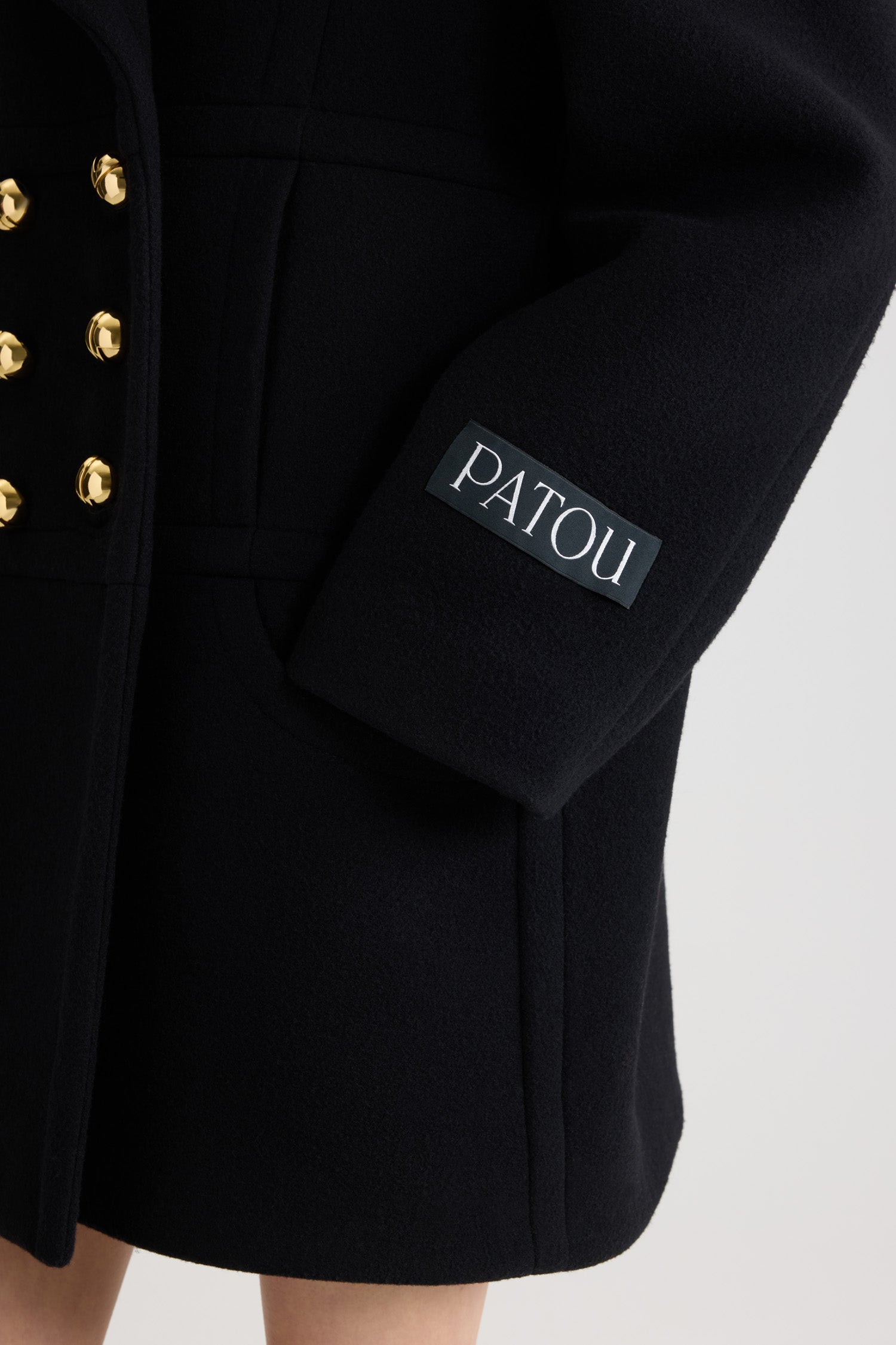 Patou - Cappotto doppiopetto in misto lana sostenibile - Black - Cappotto in misto lana sostenibile nero. Lunghezza a mezza coscia. Silhouette dritta. Costruzione doppiopetto. Ampi rever a lancia. Bottoni oro semisferici con monogramma JP. Cuciture curve sul davanti. Tasche integrate nelle cuciture. Etichetta con logo Patou sulla manica sinistra. Modello foderato.