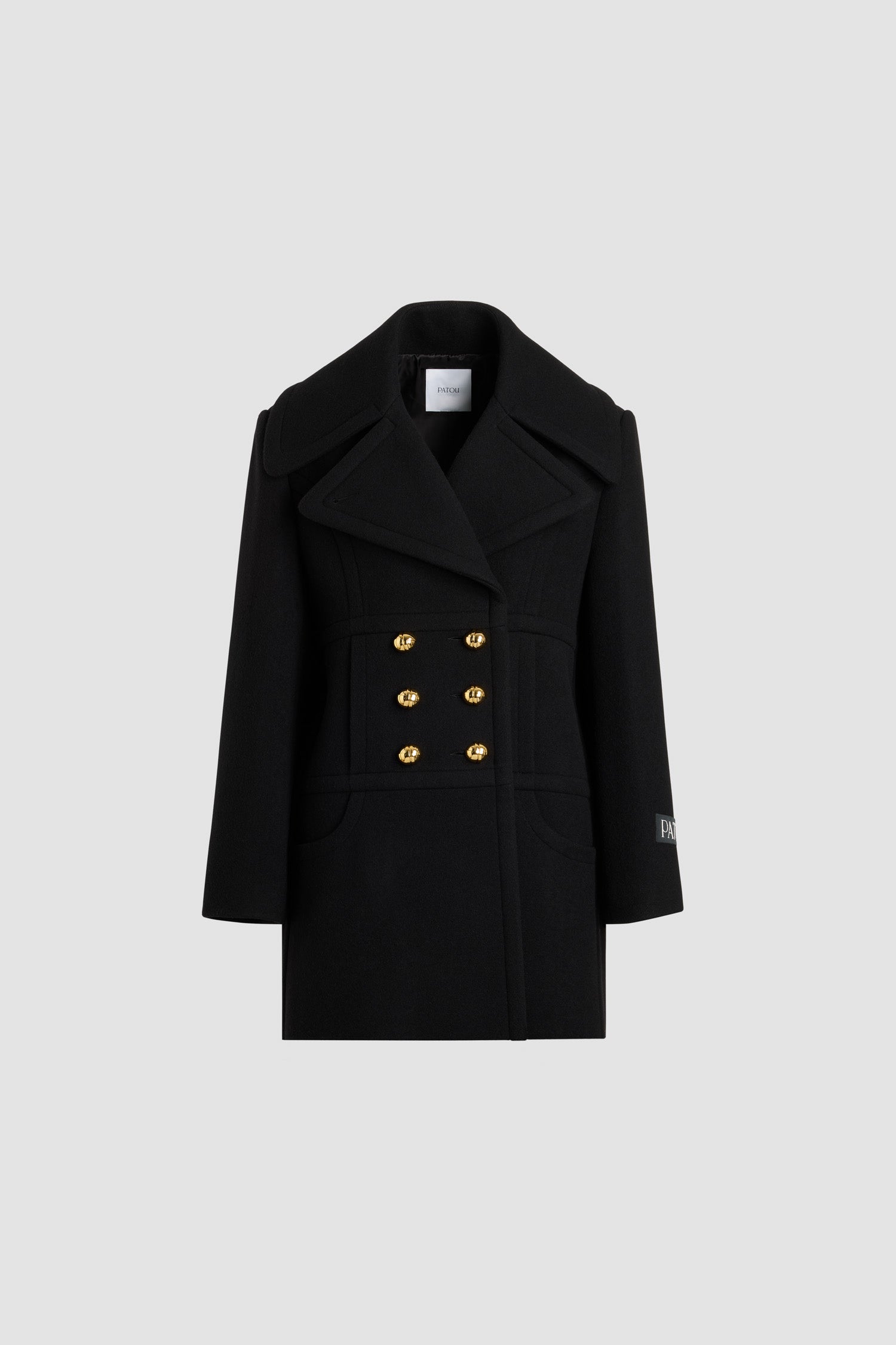 Patou - Cappotto doppiopetto in misto lana sostenibile - Black - Cappotto in misto lana sostenibile nero. Lunghezza a mezza coscia. Silhouette dritta. Costruzione doppiopetto. Ampi rever a lancia. Bottoni oro semisferici con monogramma JP. Cuciture curve sul davanti. Tasche integrate nelle cuciture. Etichetta con logo Patou sulla manica sinistra. Modello foderato.