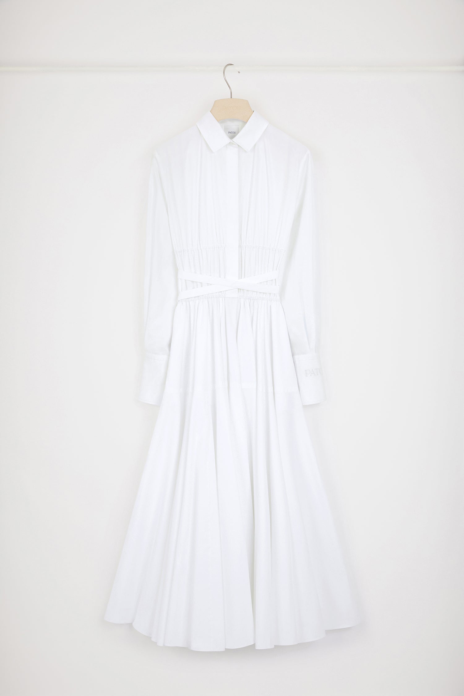 Patou - サステナブルコットン マキシ シャツドレス - White - 日々のコーデに活躍するパトゥのシャツドレスホワイトのサステナブルコットンポプリン製ドレス。マキシ丈。シャツカラー。ティアードボディス、コンシールボタン。ウエストに細い布製ベルト。袖口にボタン、左袖にPatou刺繍。ボリューム感のあるスカート。シームポケット。
