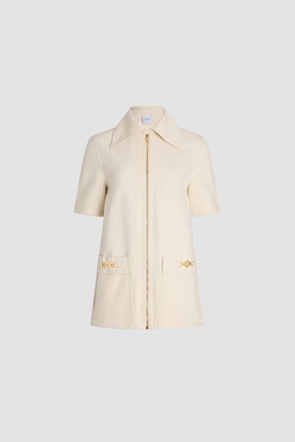 Patou - Robe courte zippée en denim de coton - Natural - Robe en denim de coton naturel écru. Modèle court. Coupe droite. Col ample. Zip doré sur le devant. Poches plaquées avec médaillon doré gravé avec le logo Patou. Pli creux au dos.Ce modèle est très court.