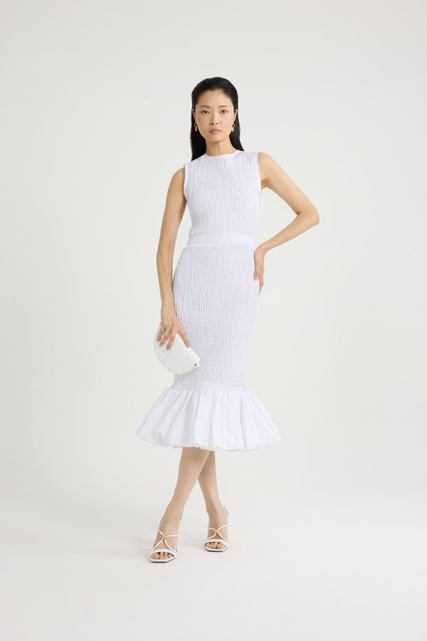 Patou - Robe midi smockée à ourlet volanté en faille recyclé - White - Robe en faille recyclée blanche. Longueur midi. Silhouette ajustée. Modèle sans manches. Zip doré au dos. Taille élastiquée. Ourlet volanté. Cette robe fait partie de la collection Cérémonie créée pour les occasions spéciales.