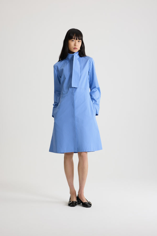 Patou - Robe chemise à col foulard en popeline de coton bio - Ice Blue Stripes - Robe en coton bio bleu glacier. Motif rayé. Longueur genou. Silhouette ajustée et évasée. Col foulard avec à l’avant. Fermeture par bouton dissimulé à l’avant. Logo Patou brodé à la taille. Poignets boutonnés. Poches latérales.