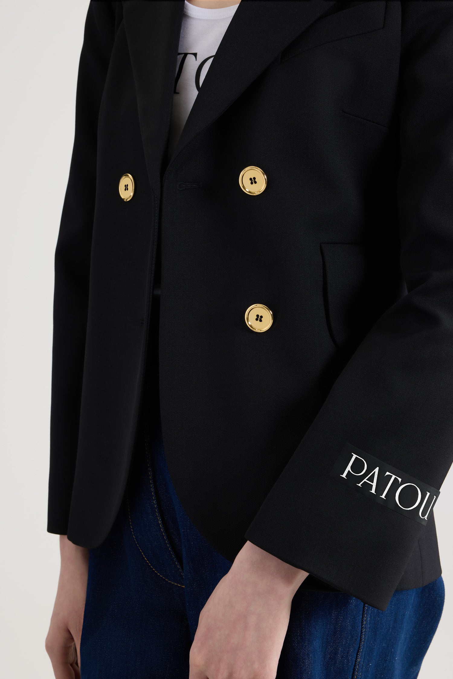 Patou - Taillierte Jacke mit Gürtel aus nachhaltiger technischer Wolle - Black - Schwarze Jacke aus nachhaltigem technischem Wolltwill. Doppelreihig geknöpft. Jackett-Silhouette. Fallendes Revers. Goldfarbene Knöpfe mit Patou Logogravur. Taillengürtel aus Stoff. Pattentaschen. Verkürzte Ärmel. Patou Logoetikett auf dem linken Ärmel.