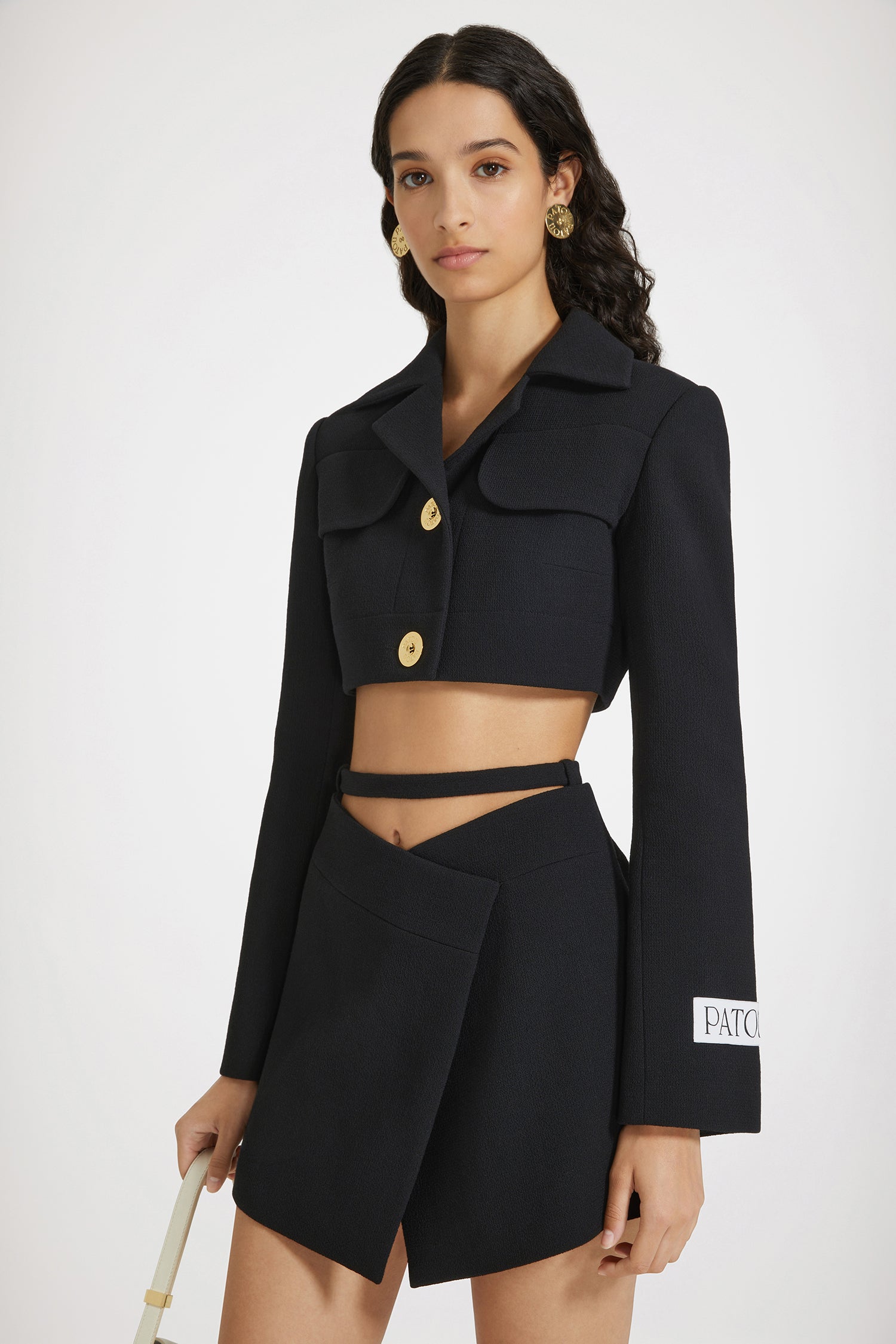 Patou - Giacca cropped in crepe di lana - Black - Il tailoring contemporaneo in versione corta.Giacca in doppio crepe di lana nero. Modello corto. Rever classico. Tasche con patta al petto. Bottoni oro incisi Patou. Polsini abbottonati. Etichetta Patou sulla manica sinistra. Modello foderato.Questo modello è cropped.