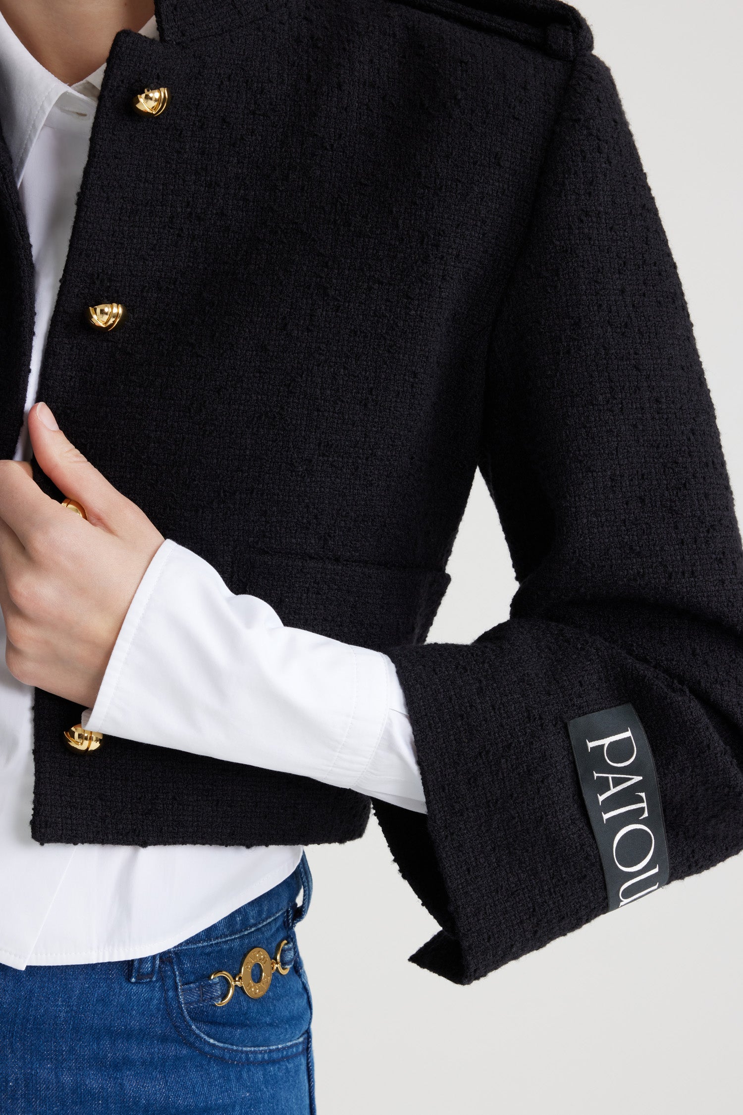 Patou - サステナブルウール&オーガニックコットンツイード クロップド セーラージャケット - Black - ブラックのサステナブル ウール&オーガニックコットン製ツイード ジャケット。クロップド丈。ワイドカラー。ゴールドトーンの半球型JPボタン。ボタン付きショルダータブ。ウェルトポケット付き。ややクロップドスリーブ。袖口にボタン付き。左袖にパトゥラベル。裏地付き。フィット感のあるショートスタイル。