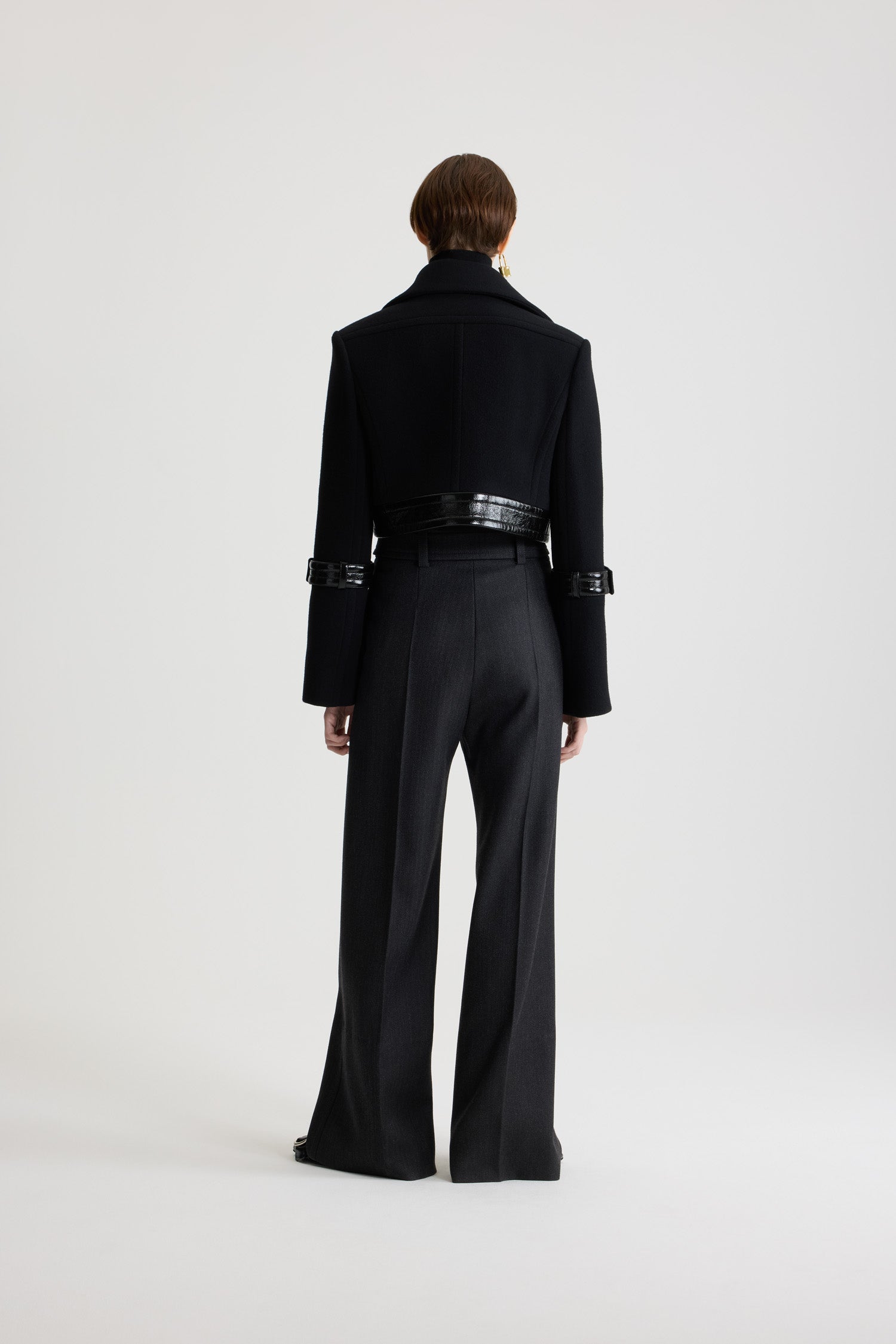 Patou - サステナブル ウールブレンド クロップド ロックジャケット - Black - ブラックのサステナブル ウール混紡ジャケット。丈の短いシルエット。シングルブレストスタイル。ワイドカラー。隠しボタン留め。シルバーカラーのロック留め付きのパテントレザー製ウエストバンド。袖にパテントレザー製のボタン付きタブ。左袖にPatouロゴラベル。裏地付き。