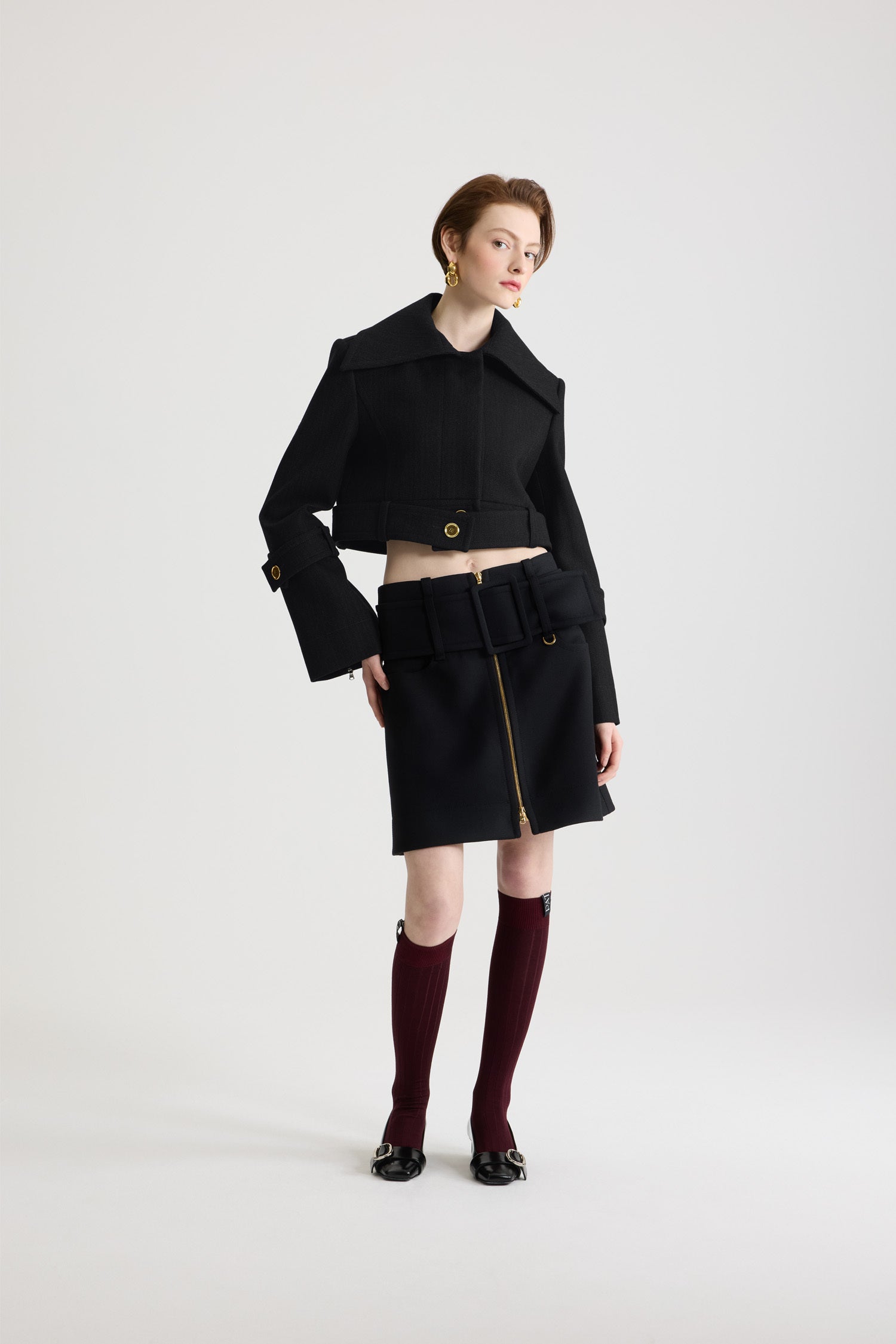 Patou - ウール ベルテッド クロップドジャケット - Black - ブラックのバージンウール製ジャケット。丈の短いシルエット。シングルブレストスタイル。ワイドカラー。シルバートーンのJP刻印入りボタン付きのコンシールボタンフロント。腰にオープンスタイルで着用可能なボタン付きベルト。やや広がった袖口にボタン付きタブ。左袖にPatouロゴラベル。裏地付き。