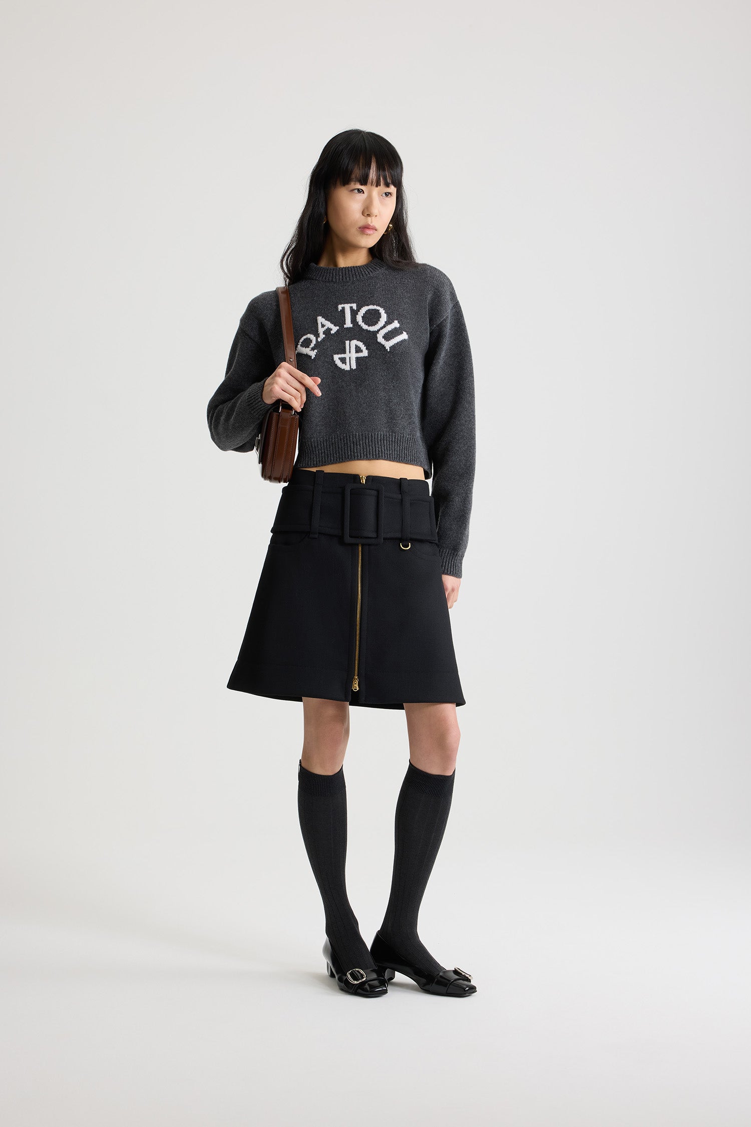 Patou - Minigonna con cintura e zip sul davanti in lana - Black - Gonna in lana nera. Modello corto. Vita bassa. Chiusura con zip oro a doppio cursore sul davanti. Cintura ampia in tessuto sui fianchi con fibbia rivestita in tessuto e D-ring oro. Tasche basse sul davanti. Modello foderato.