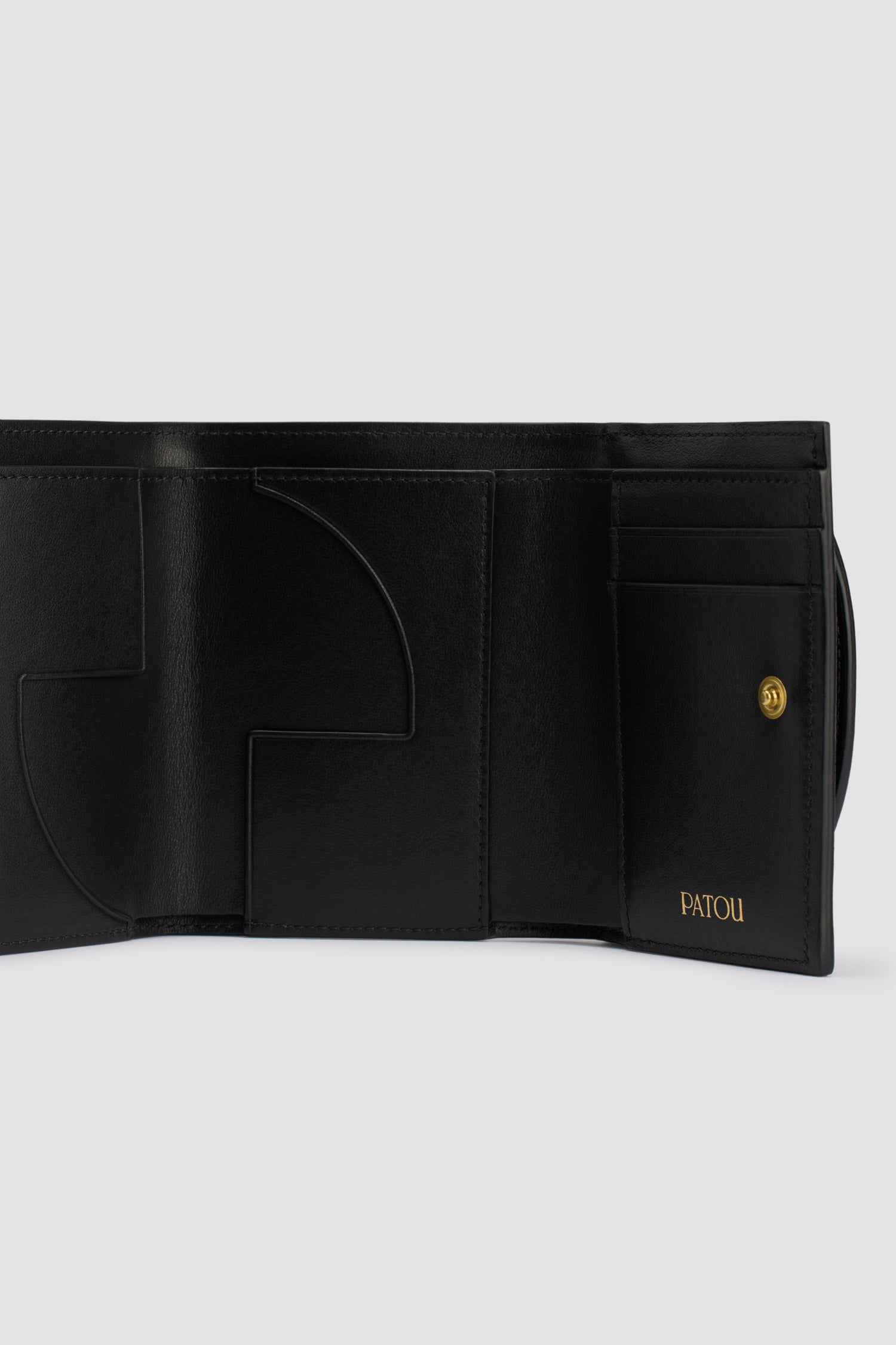 Patou - レザー JP ウォレット - Black - ブラックのレザー製ウォレット。未使用の高品質皮革を用いた独自素材を使用。前面にゴールドトーンのJP。スナップボタン開閉。カードスロット&ポケット複数、紙幣用の大きめポケット 1つ。内側にJPのカットアウトおよびゴールドエンボスのPatou。